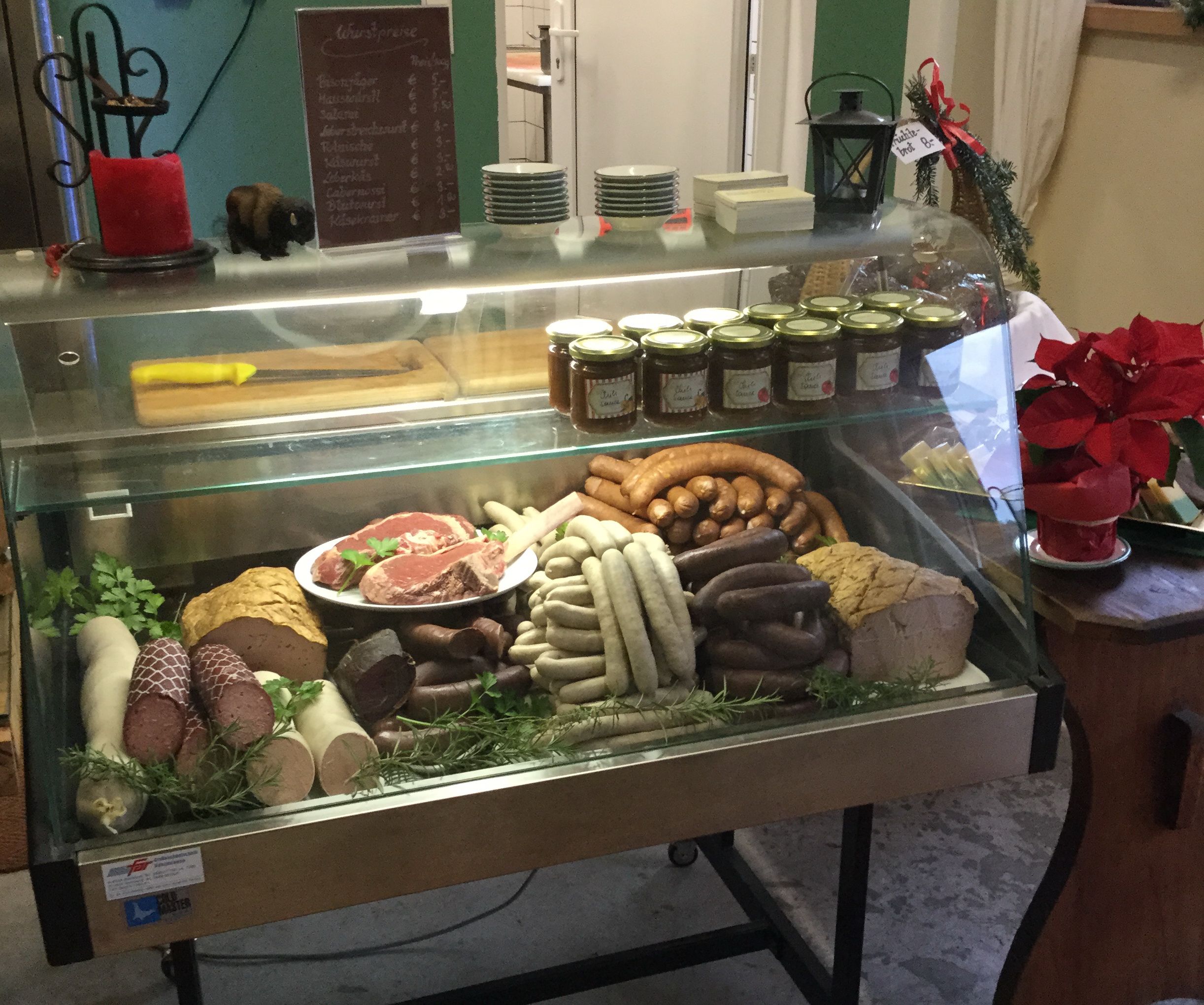 A meat counter in a farm store with different types of sausage, pieces of meat and jars of spreads.