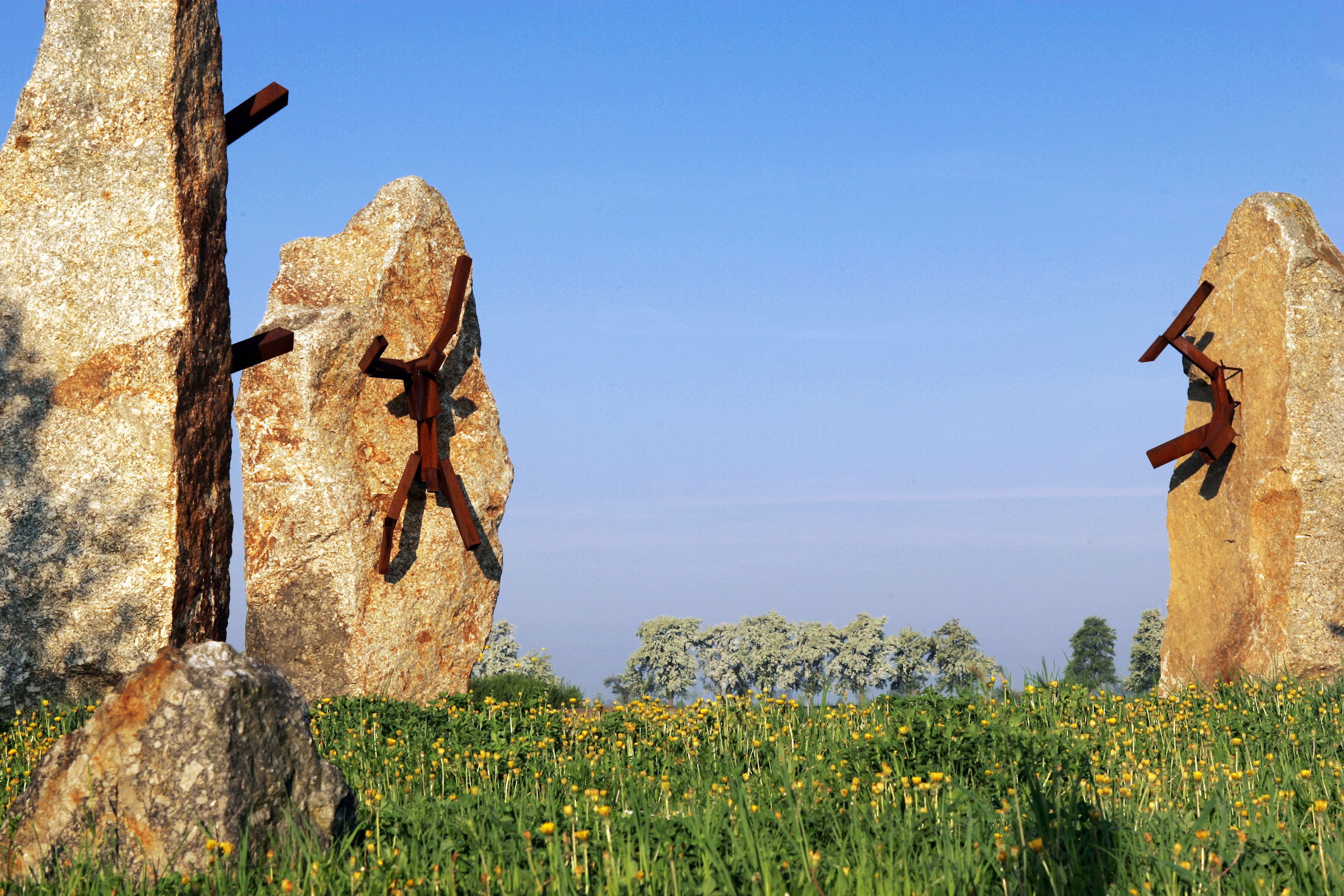 Stone sculptures with metal figures on a meadow under a blue sky.