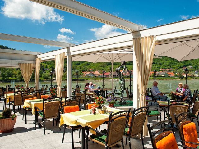 Restaurant terrace with a view of a river and green hills in the background.