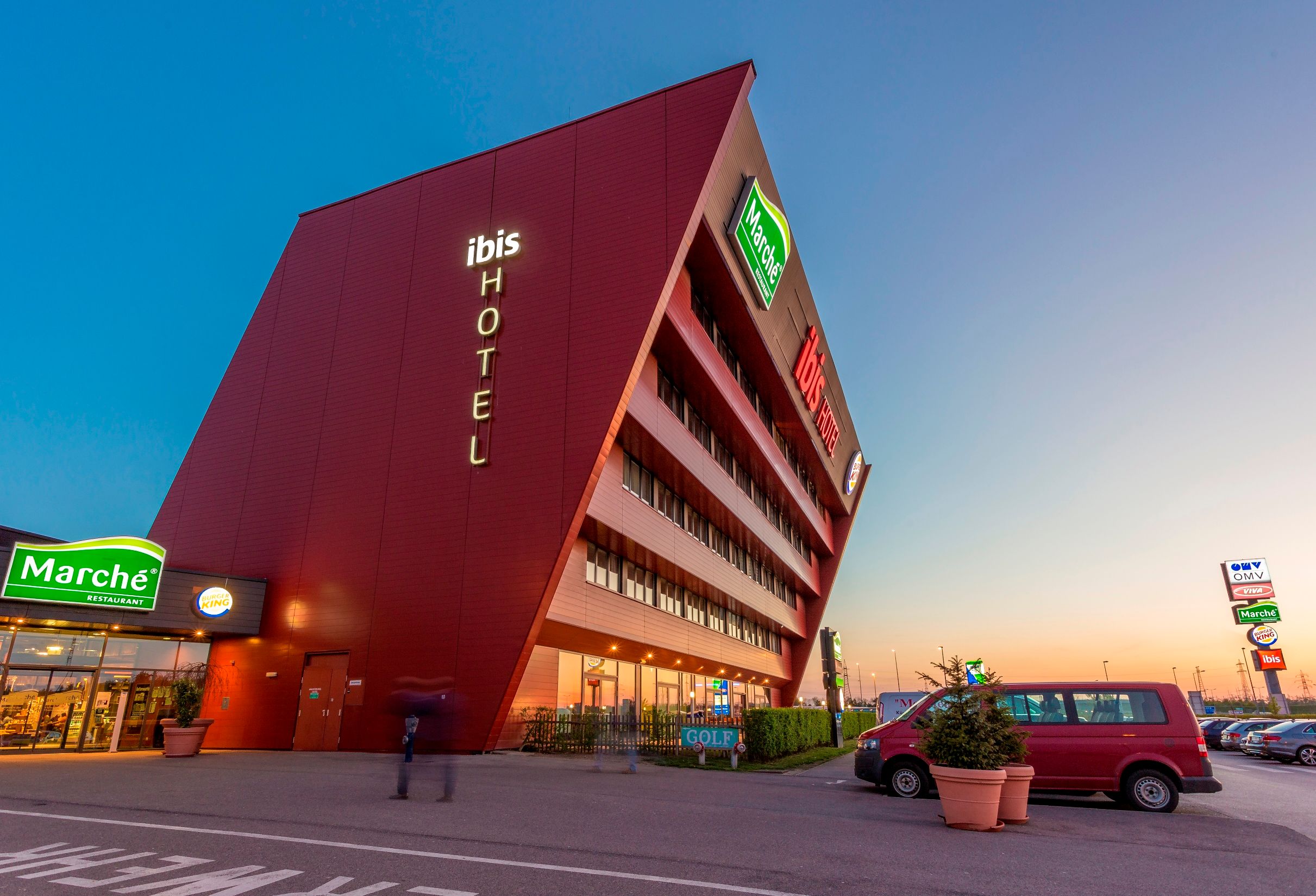 Modern hotel building with sloping façade and illuminated lettering 'ibis HOTEL'.