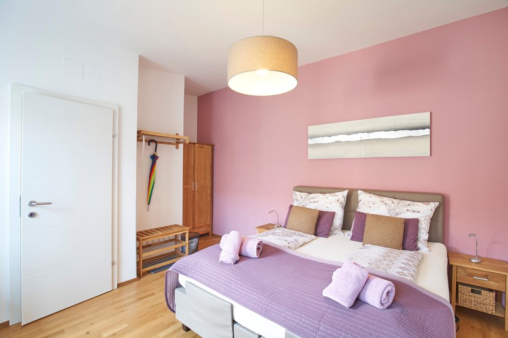 A cozy guest room with a pink wall, double bed and modern furnishings.