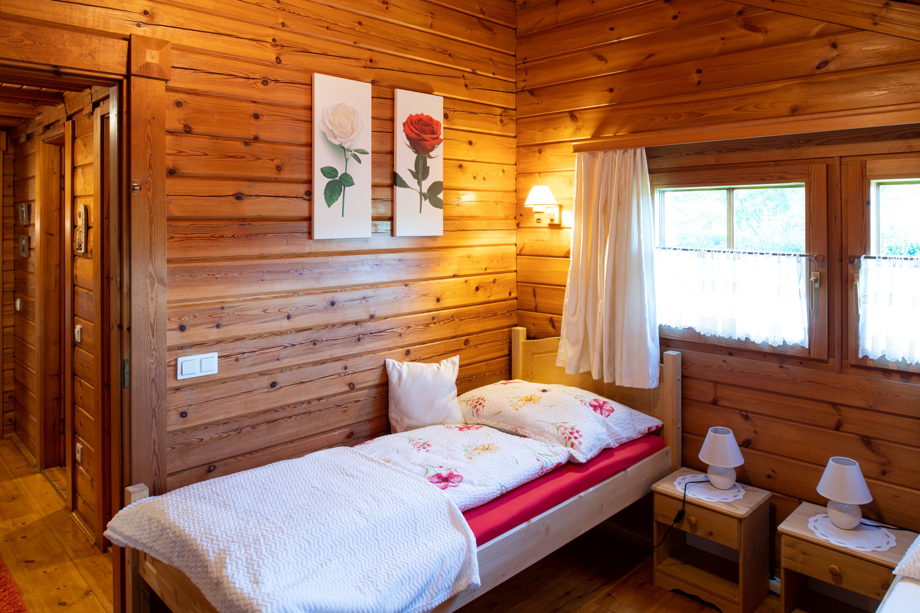 Cozy bedroom with wooden walls, single bed, two bedside tables and windows with curtains.