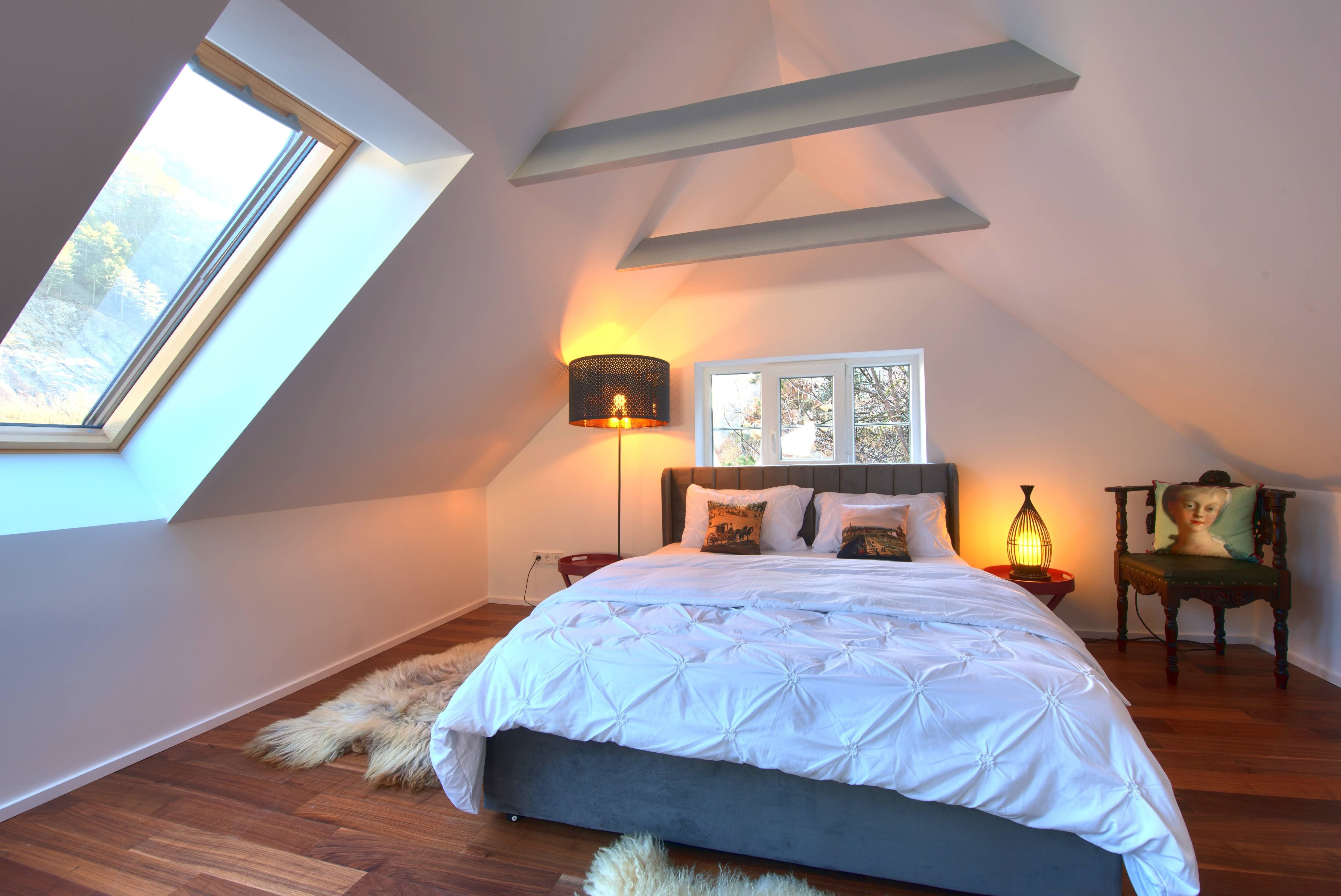 Modern bedroom with sloping ceiling, large bed, skylight and stylish lighting.