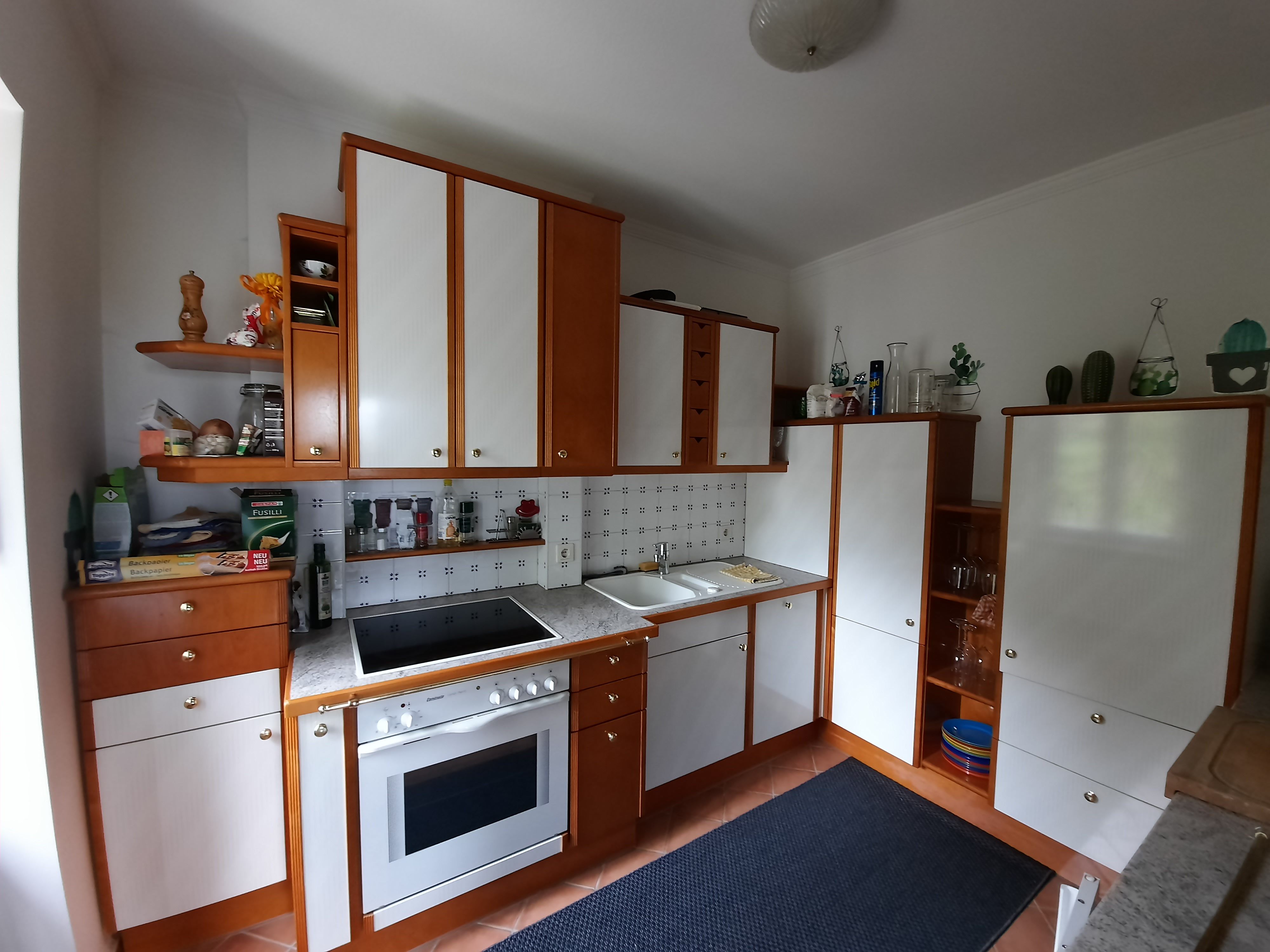 Kitchen with wooden and white cupboards, stove, sink and shelves with spices and decorations.