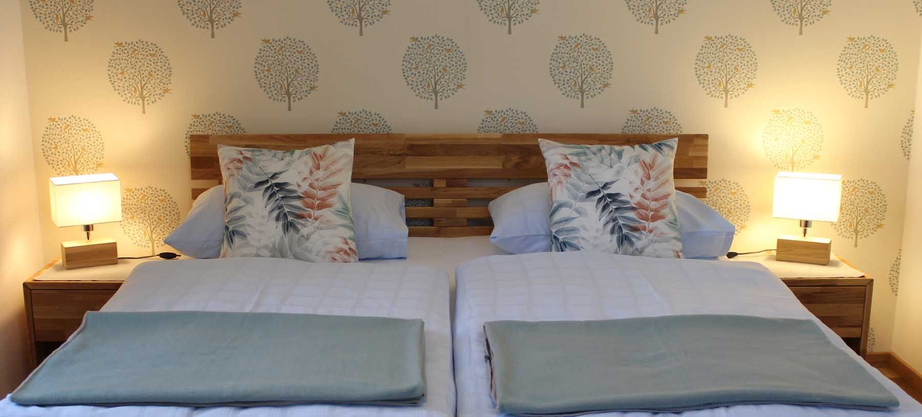 Comfortable double bed with wooden headboard, blankets and pillows and bedside tables with lamps.