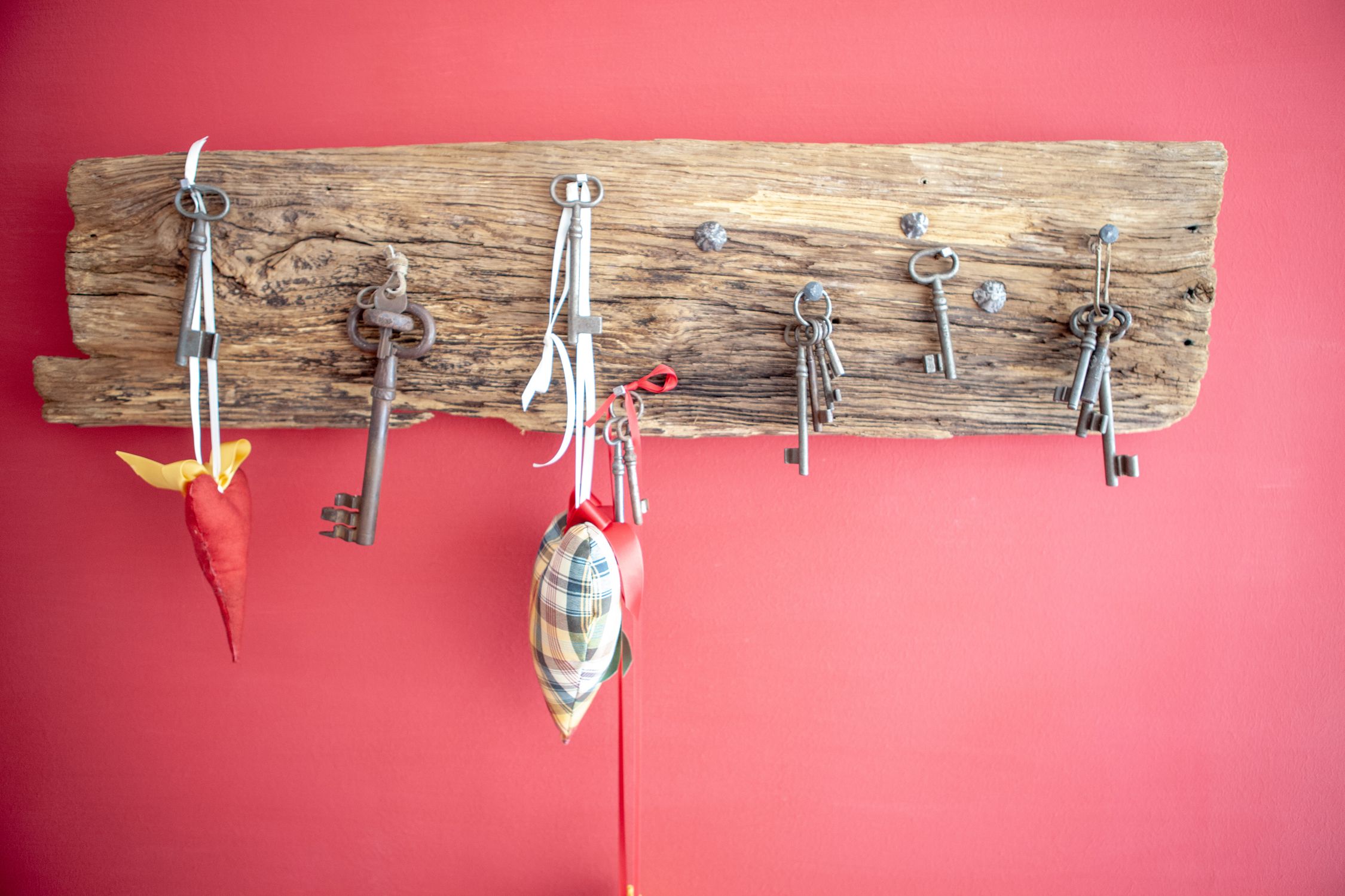 Old keys hang on a rustic wooden board in front of a red wall.
