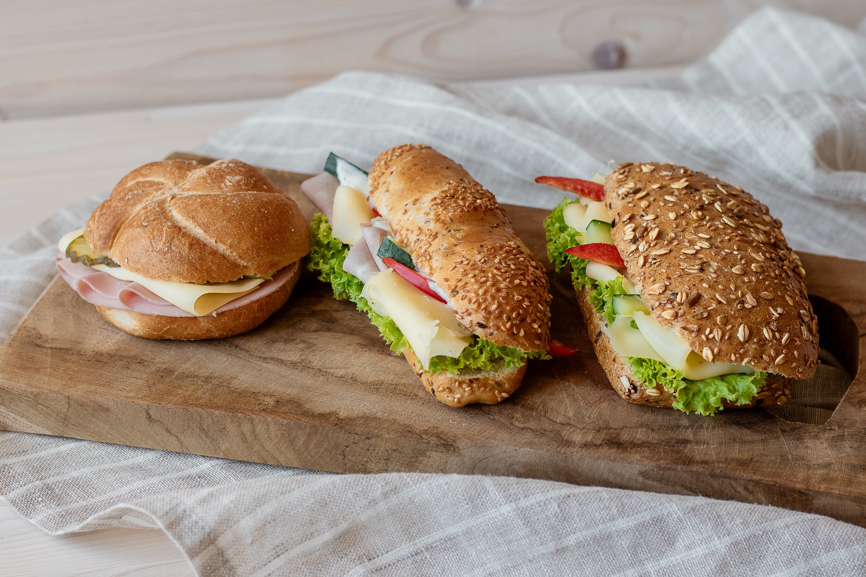 Three sandwiches on a wooden board, with cheese, ham and salad.