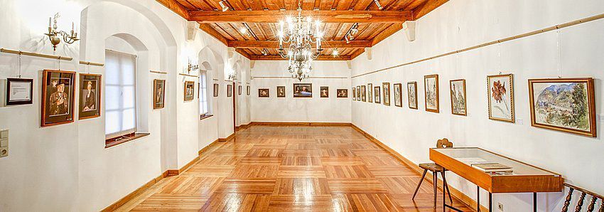 An elegant showroom with a wooden floor, white walls and paintings on the walls.