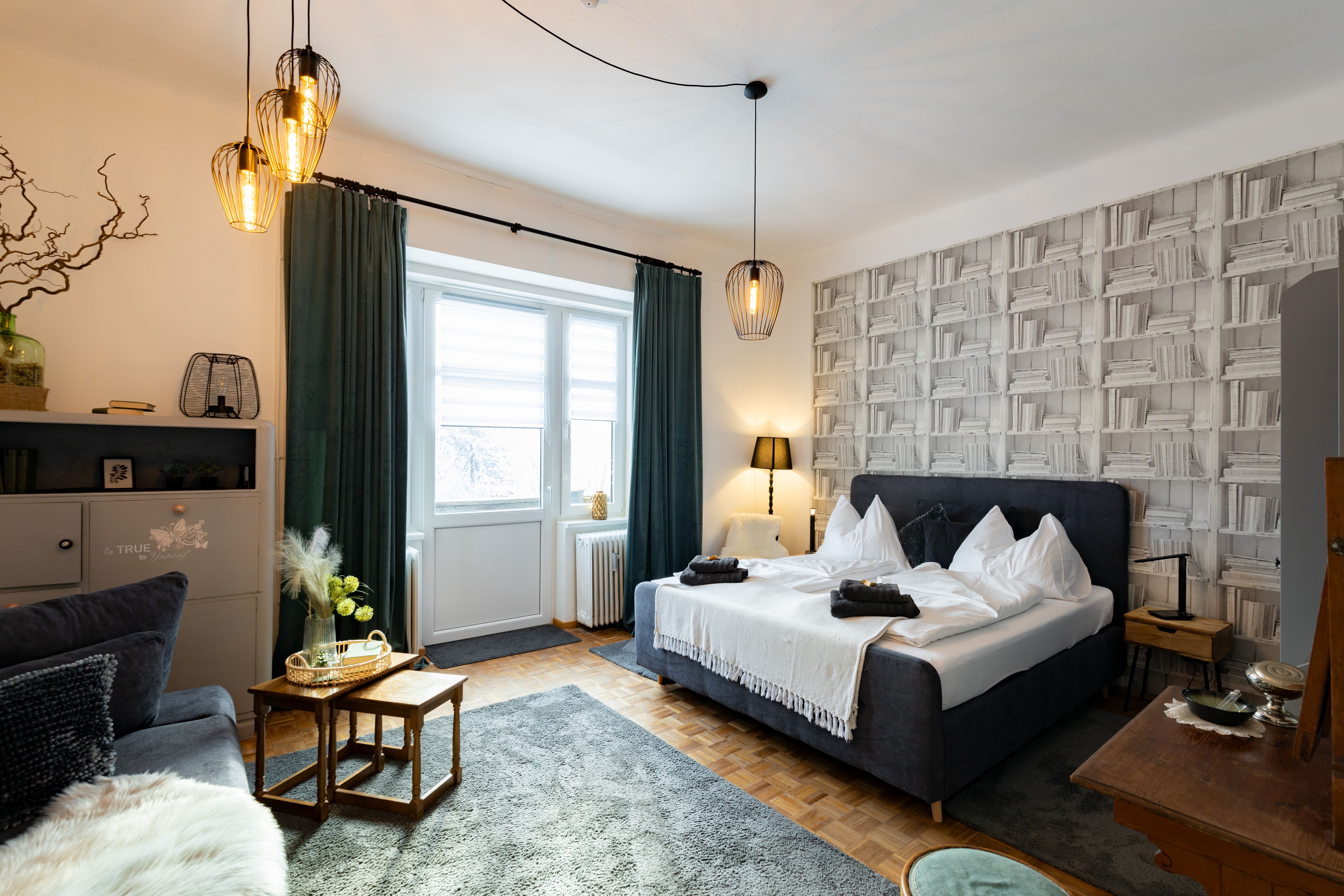 Cozy bedroom with double bed, decorative lamps and bookshelf wallpaper.