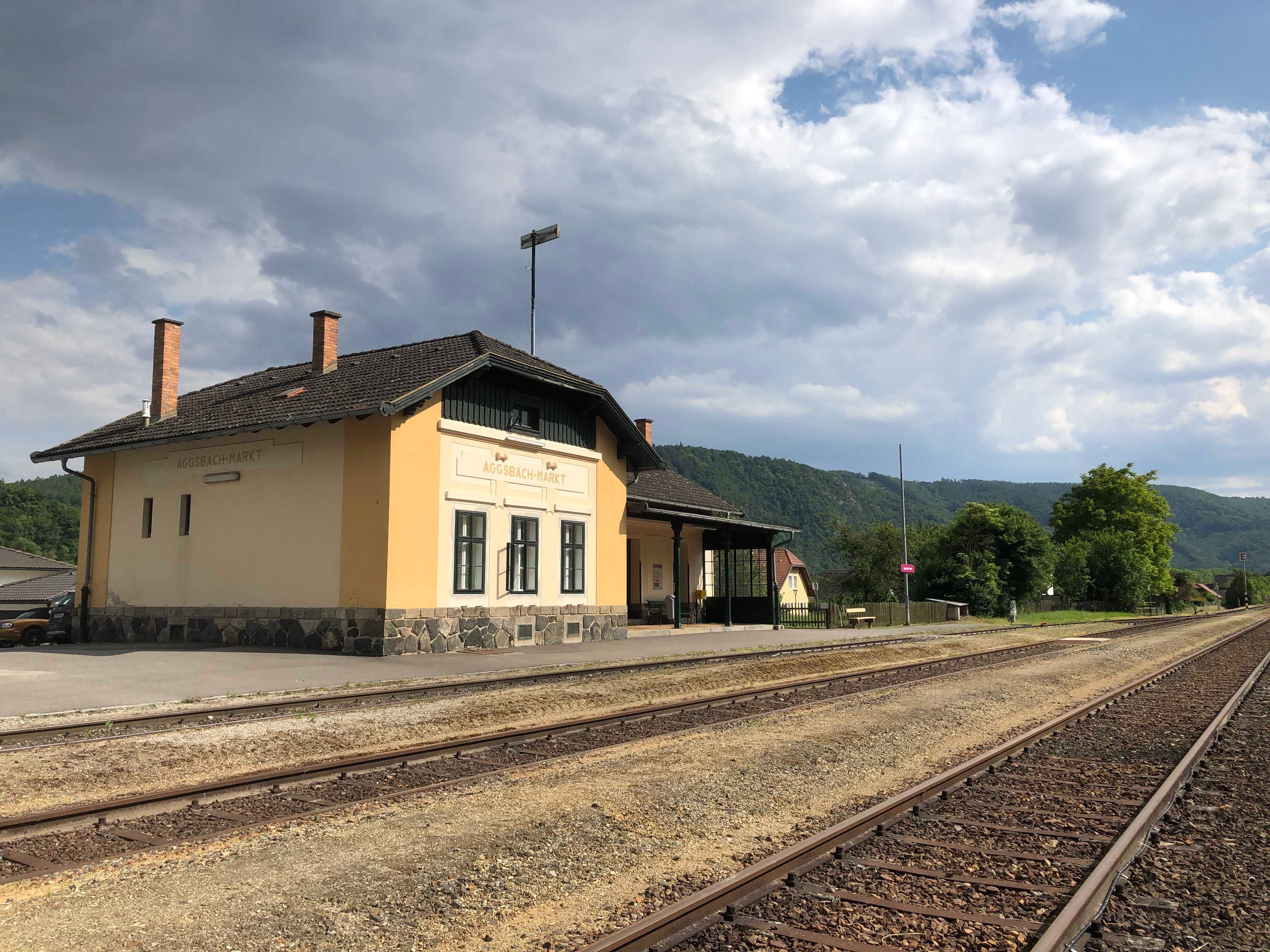 Aggsbach-Markt station with tracks and cloudy sky.