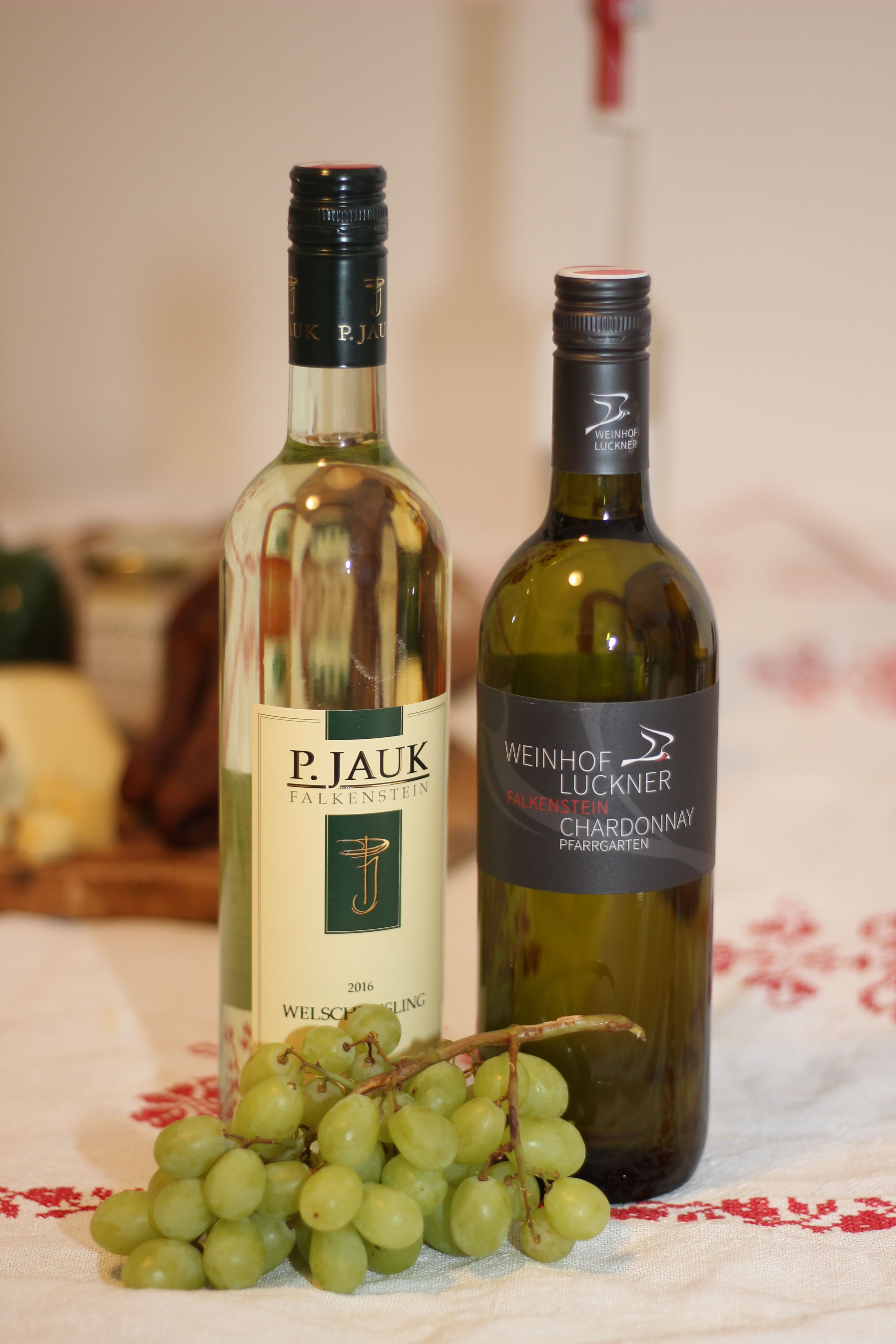 Two bottles of wine and a bunch of green grapes on a table.