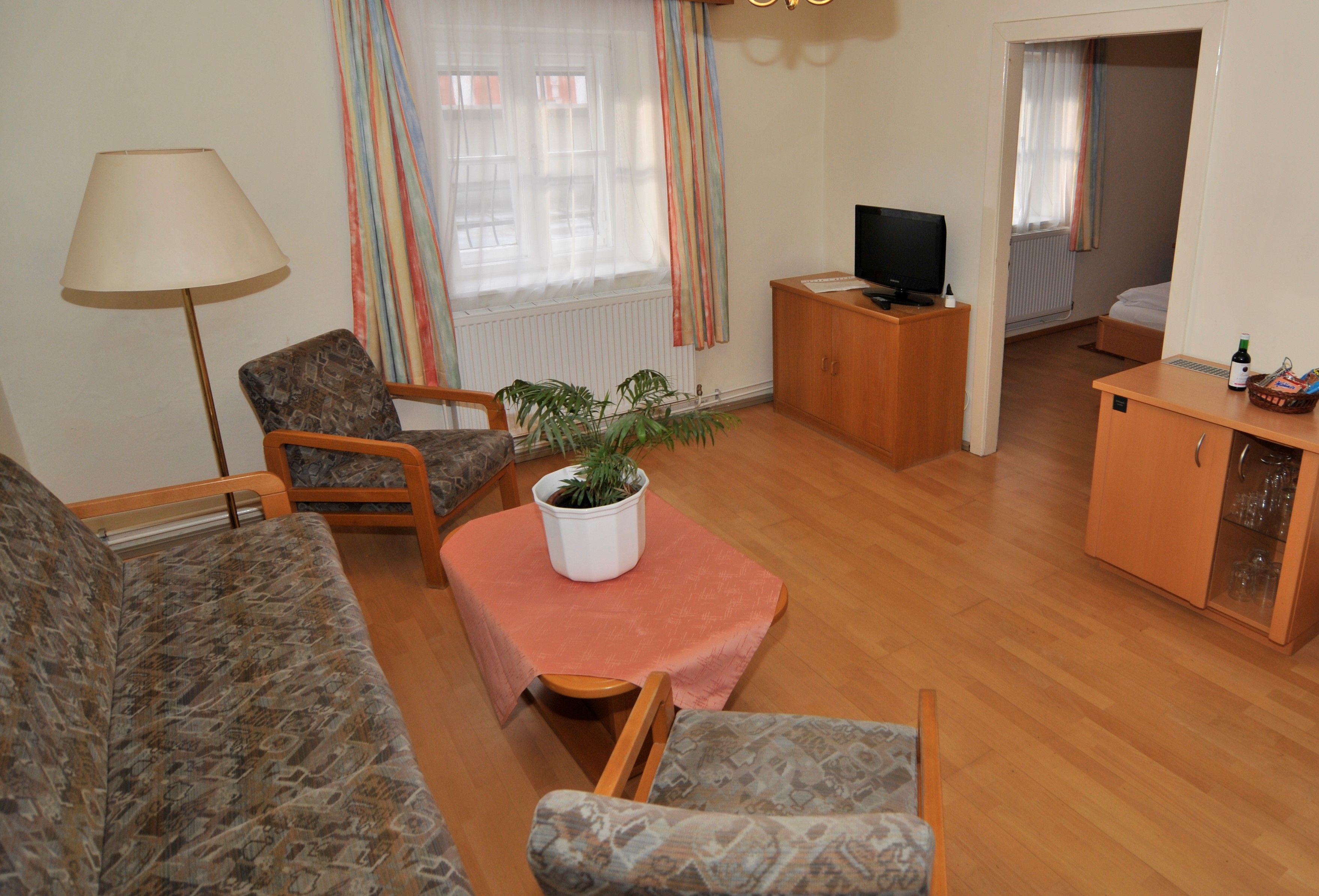 Living room with sofa, two armchairs, table with plant, TV and access to a bedroom.