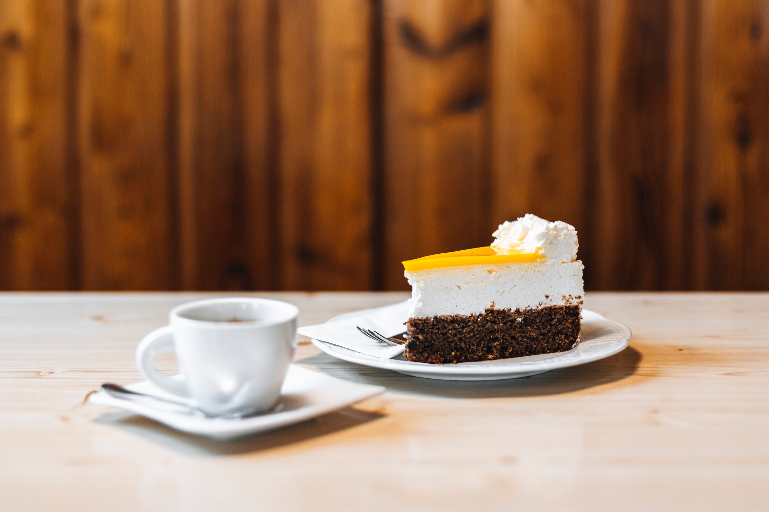 Piece of cake with cream and cup of coffee on a wooden table.