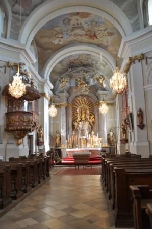 Interior view of a baroque church with altar, pulpit and chandeliers.