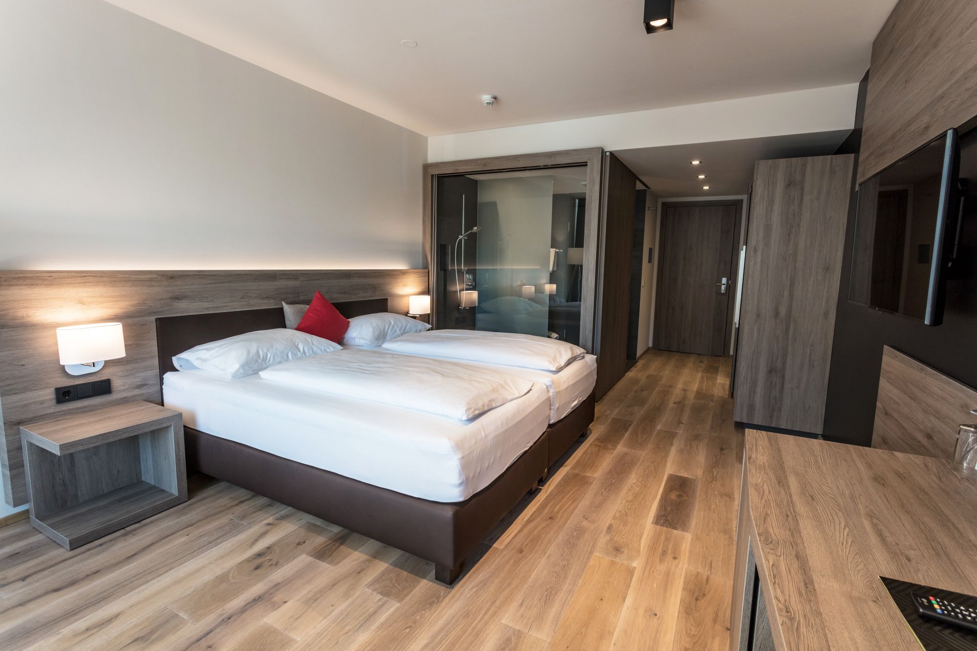 Modern hotel room with double bed, wooden floor and glass shower.