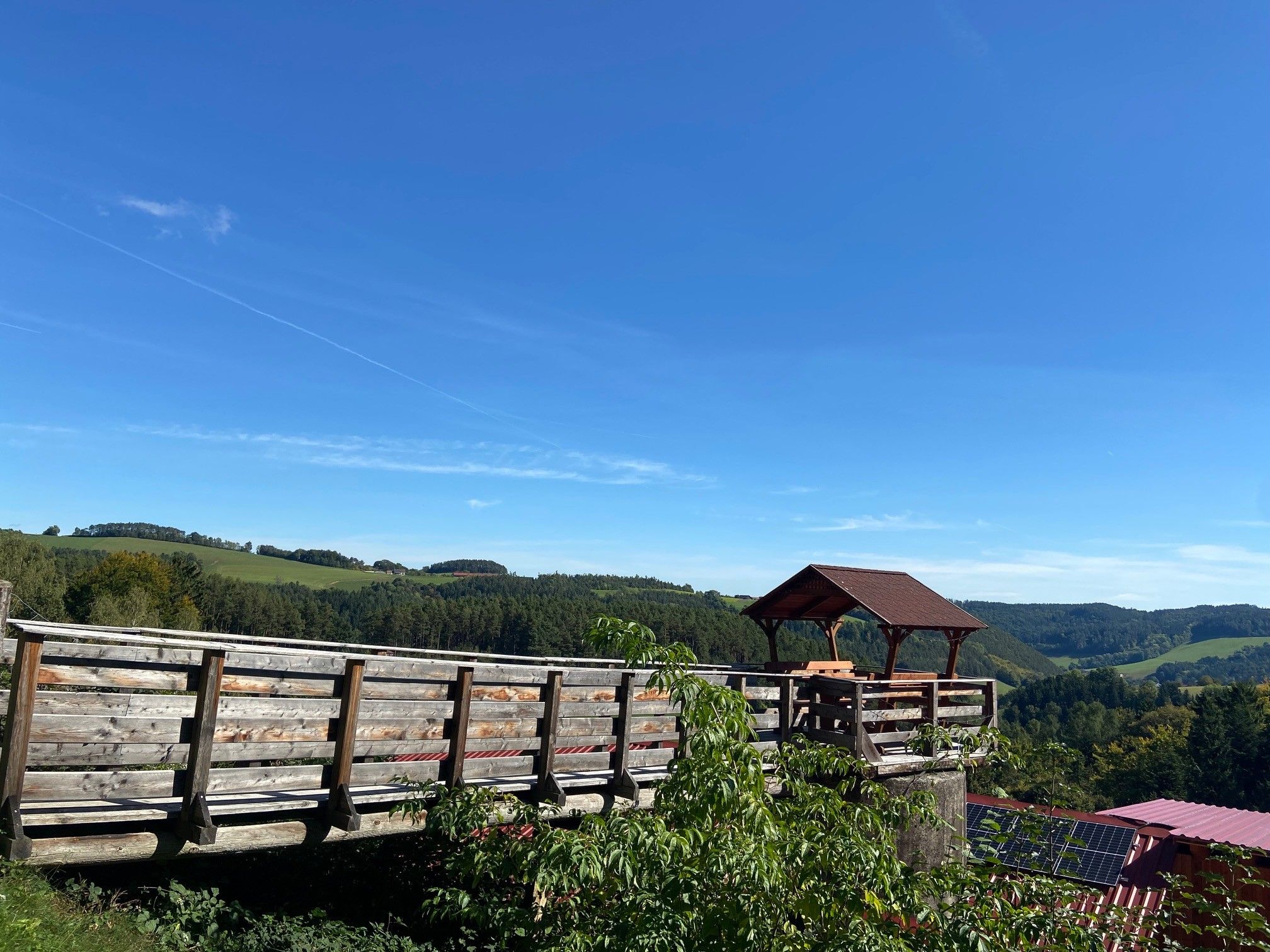 Wooden platform with pavilion and view of green hills and blue sky.
