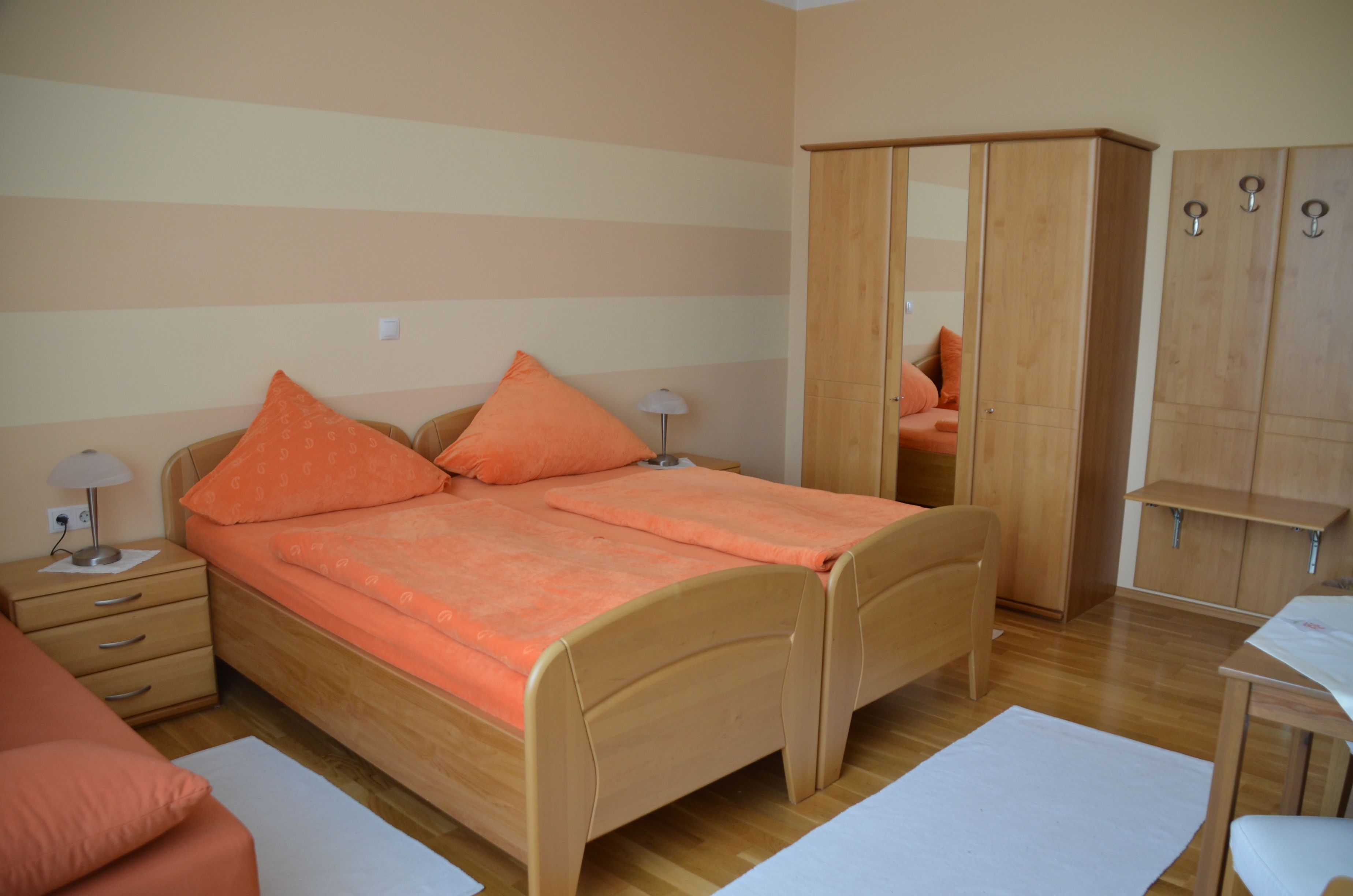 A cozy bedroom with two single beds, orange bed linen, a closet and bedside tables.