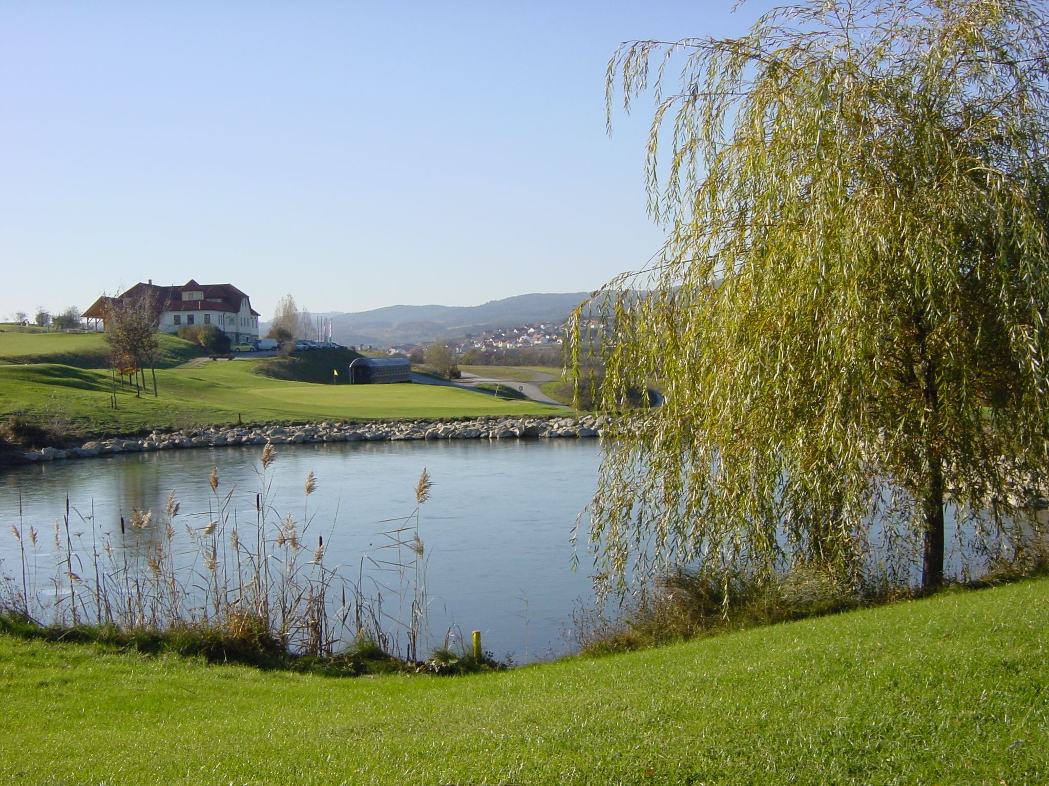 Landscape with golf course, pond and buildings in the background.