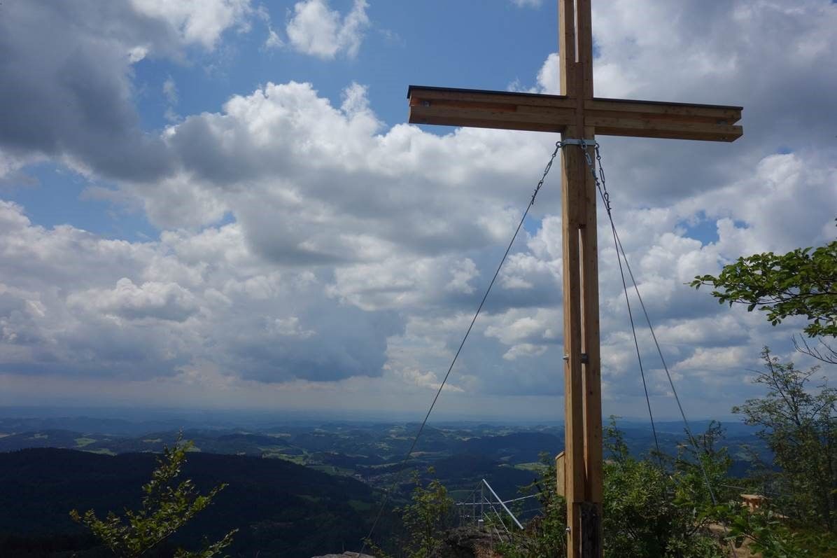 Summit cross on the Burgsteinmauer viewing mountain with a view of the cloudy sky and landscape.