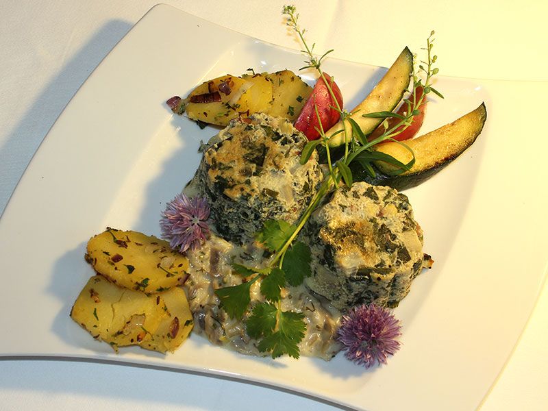 A plate of spinach dumplings, potatoes and vegetables arranged decoratively.