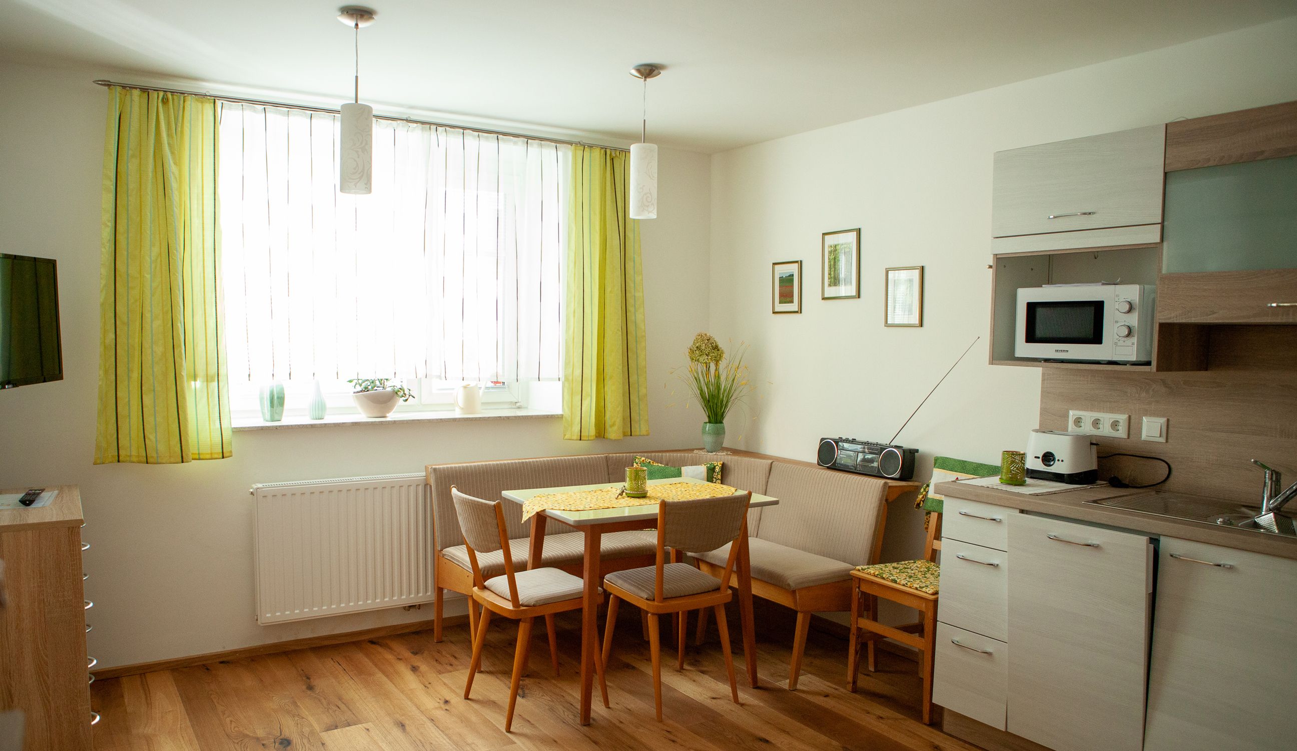 Cozy eat-in kitchen with dining table, corner bench, kitchenette and green curtains.