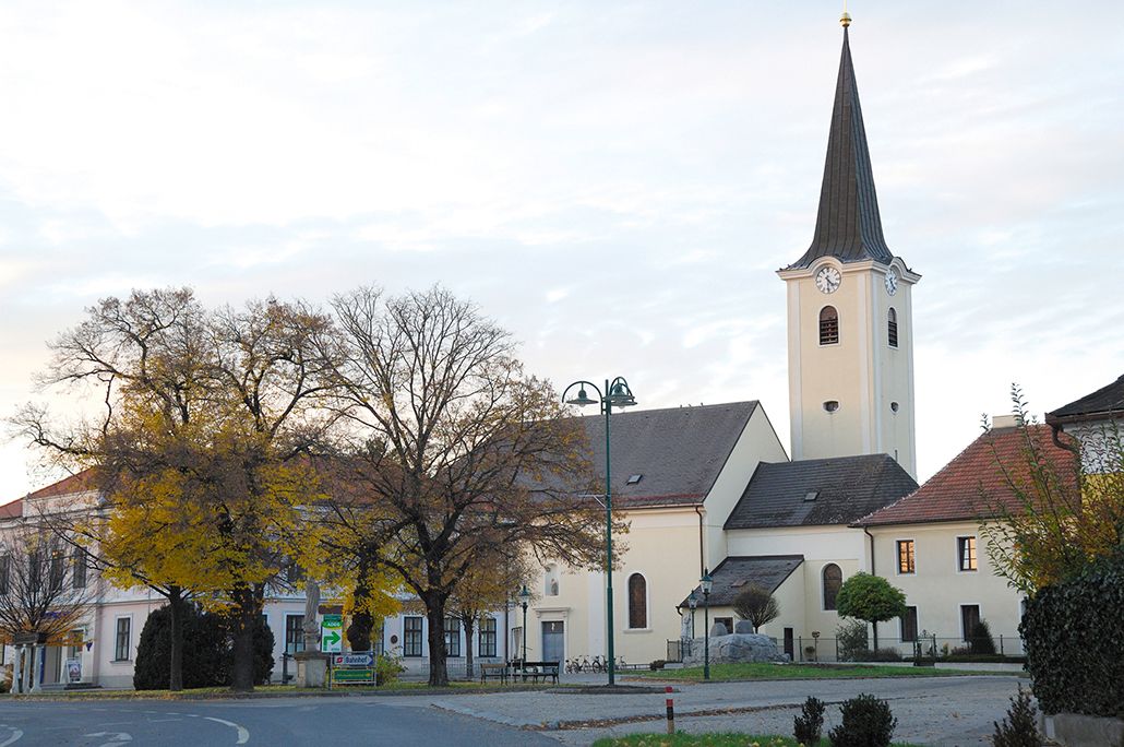 Church in Absdorf with clock tower and surrounding buildings, trees in the foreground.