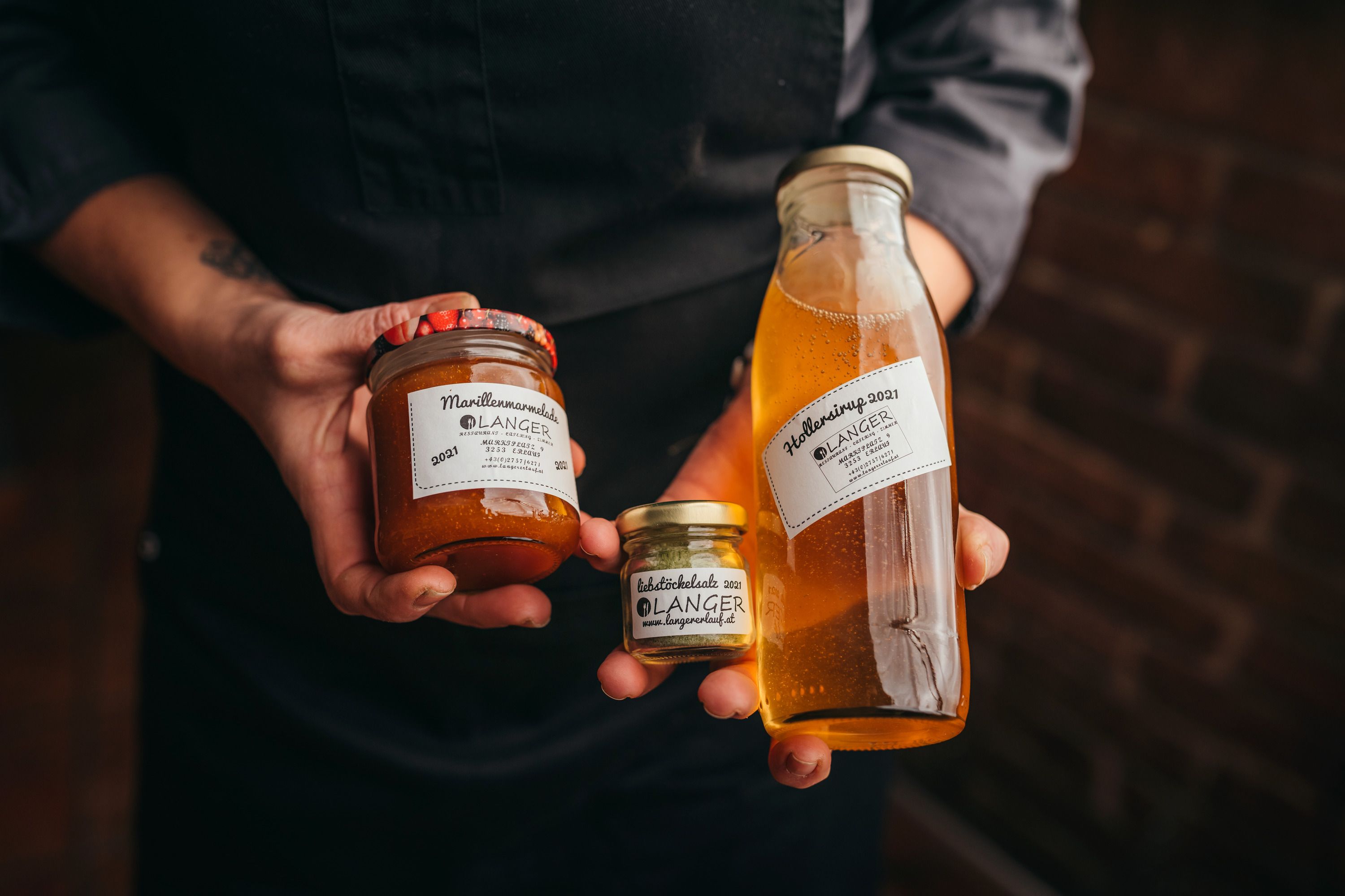 Person holding jars of apricot jam and elderberry syrup from Langer.