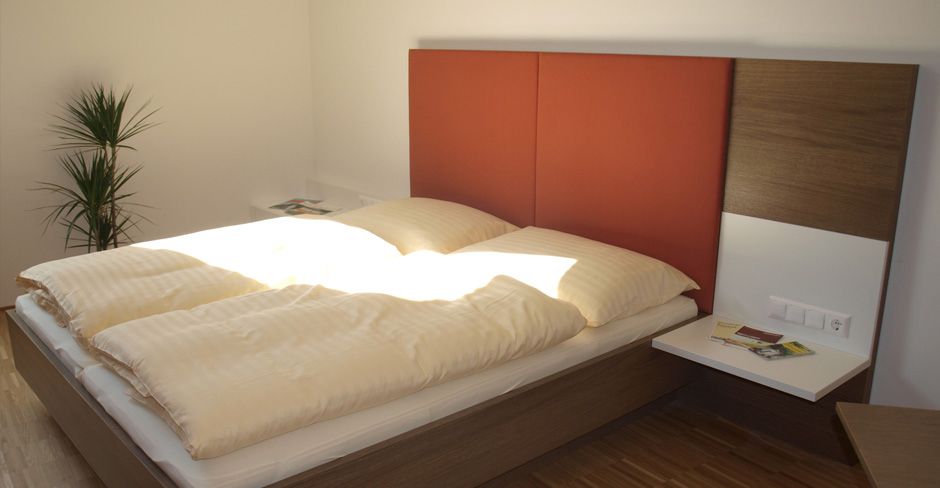 Modern guest room with double bed, red headboard and plants.