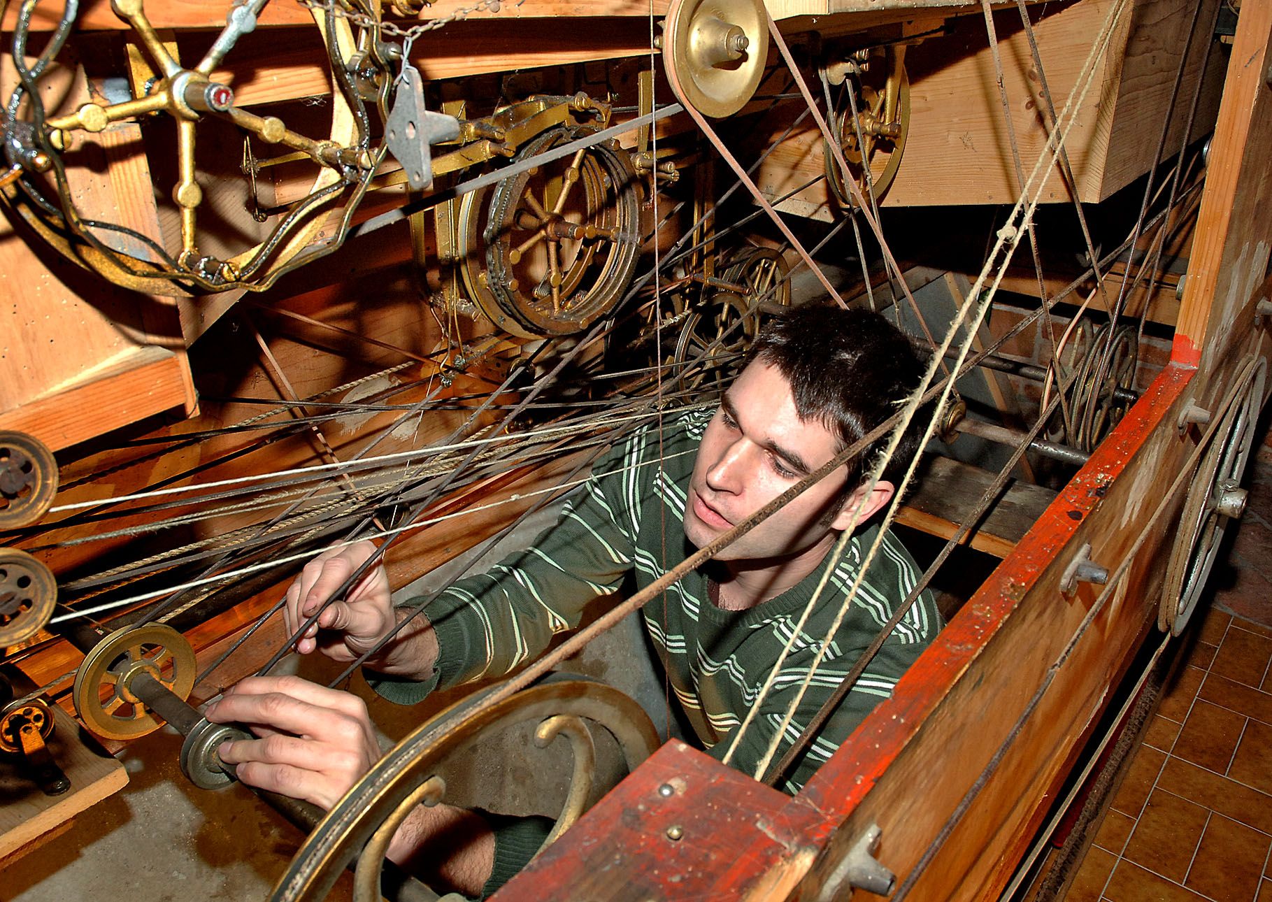 A man works on a complex system of ropes and gears in a wooden mechanism.