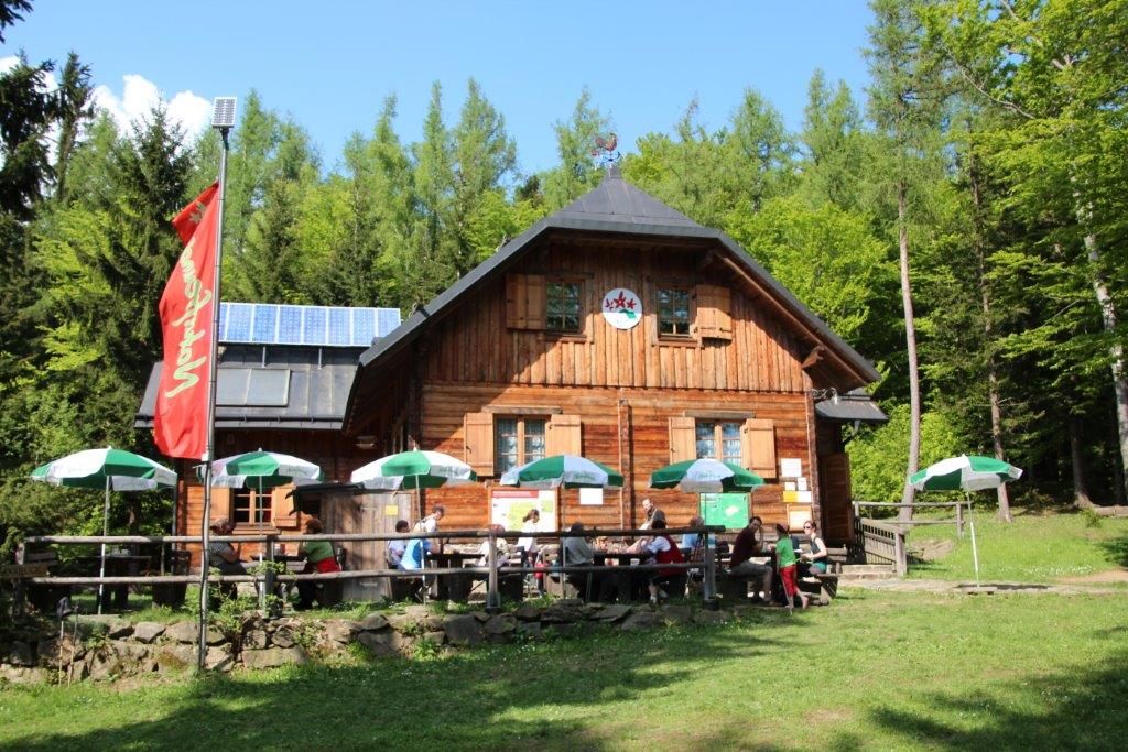 Wooden hut in the forest with parasols and people on the terrace.