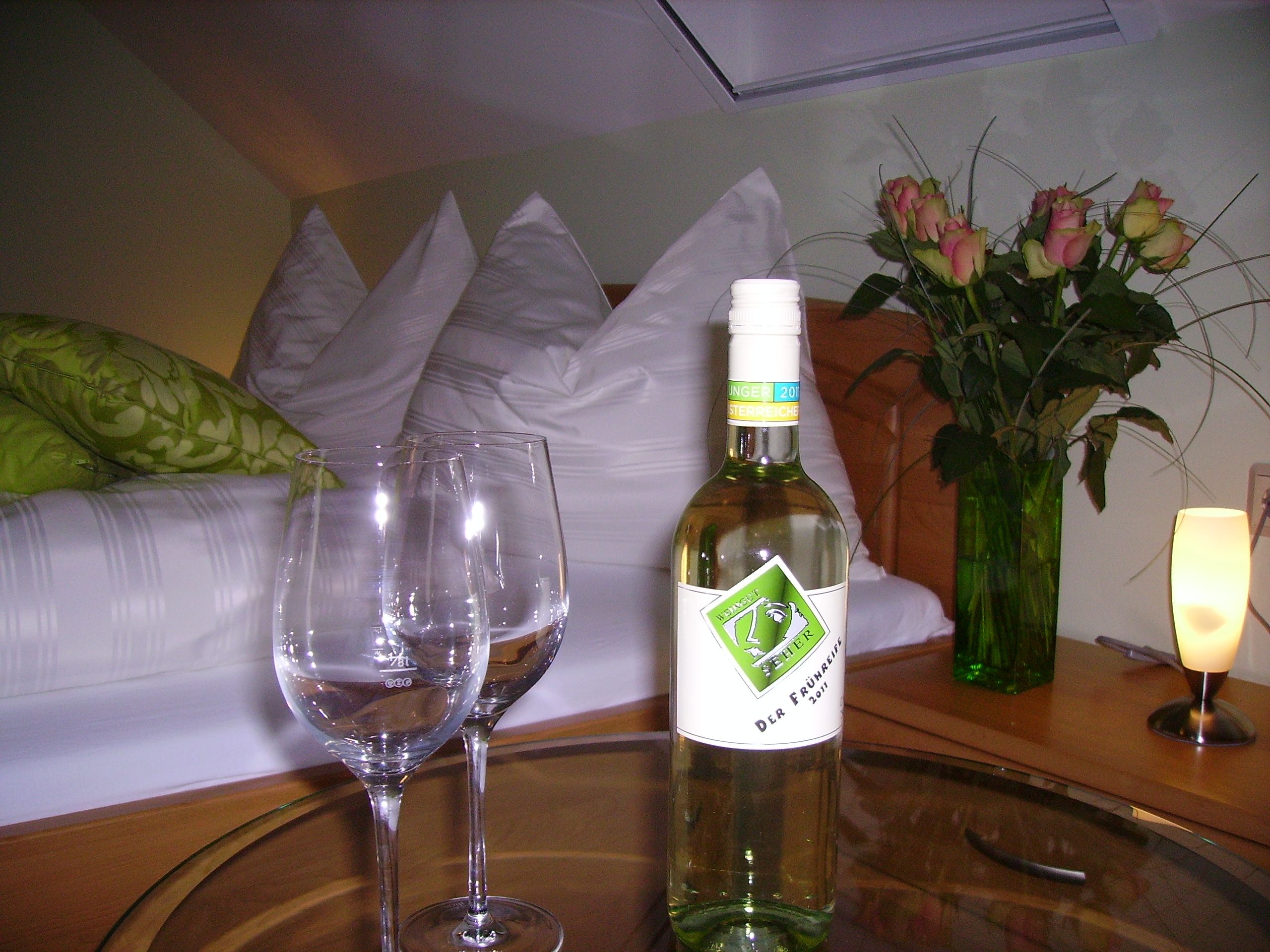 A cozy guest room with a bottle of wine, two glasses and a bouquet of flowers on a table.