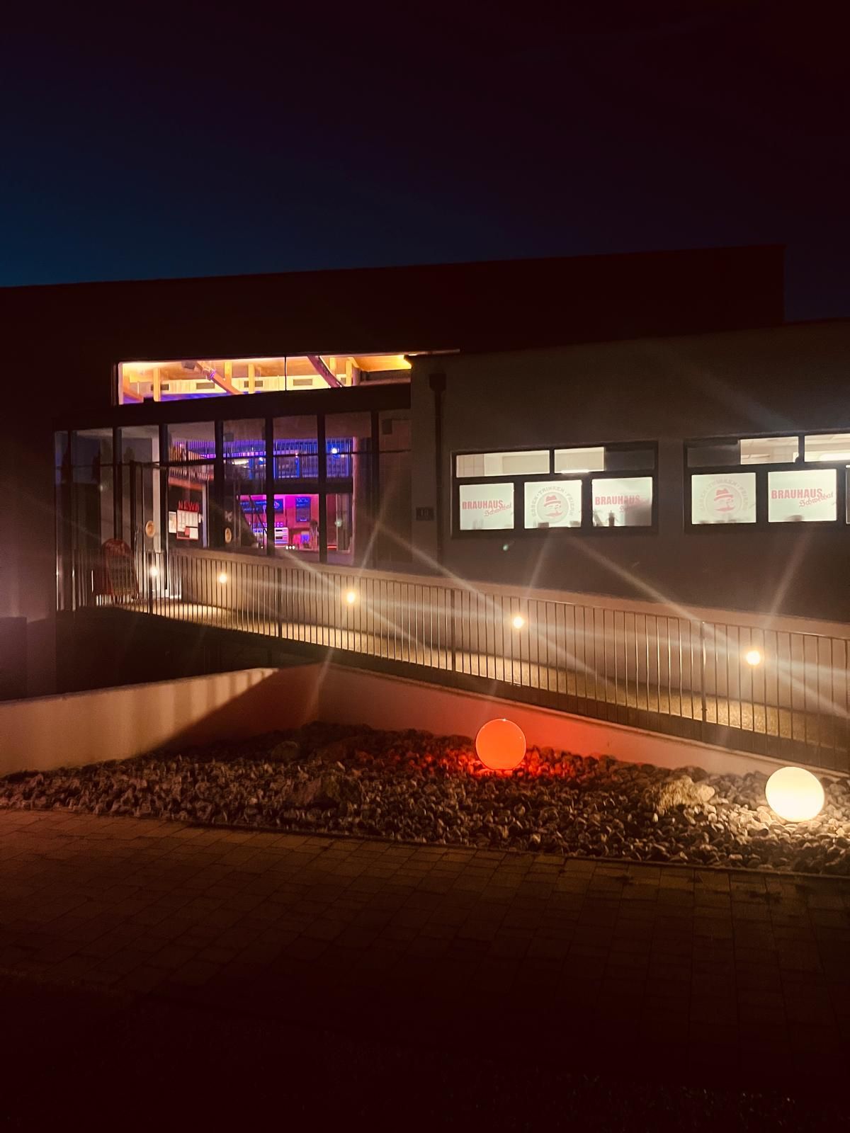 Night shot of the Schwechat brewery with illuminated windows and colored globe lights in the foreground.