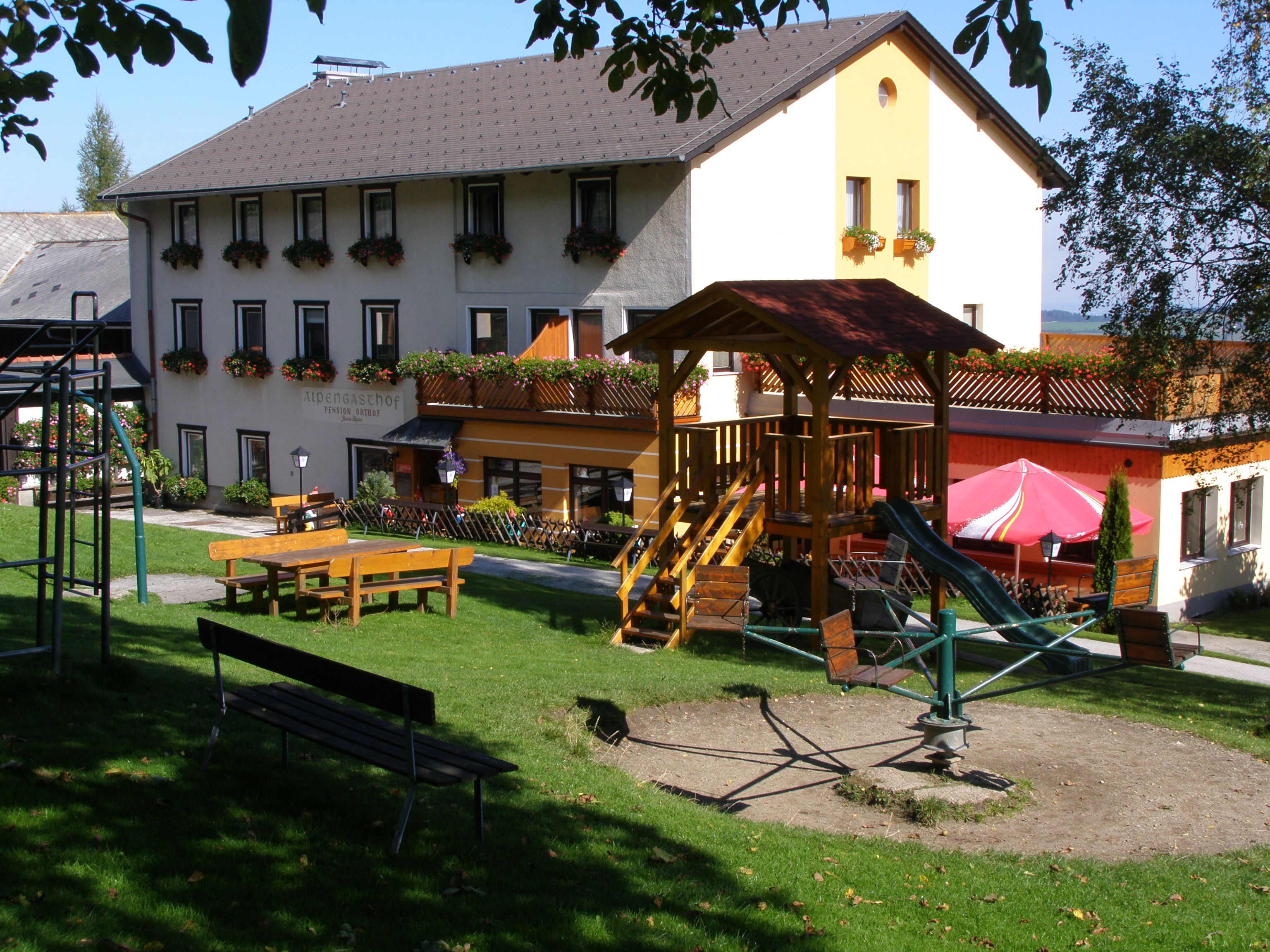 An inn with a playground in the foreground, surrounded by green meadows and trees.