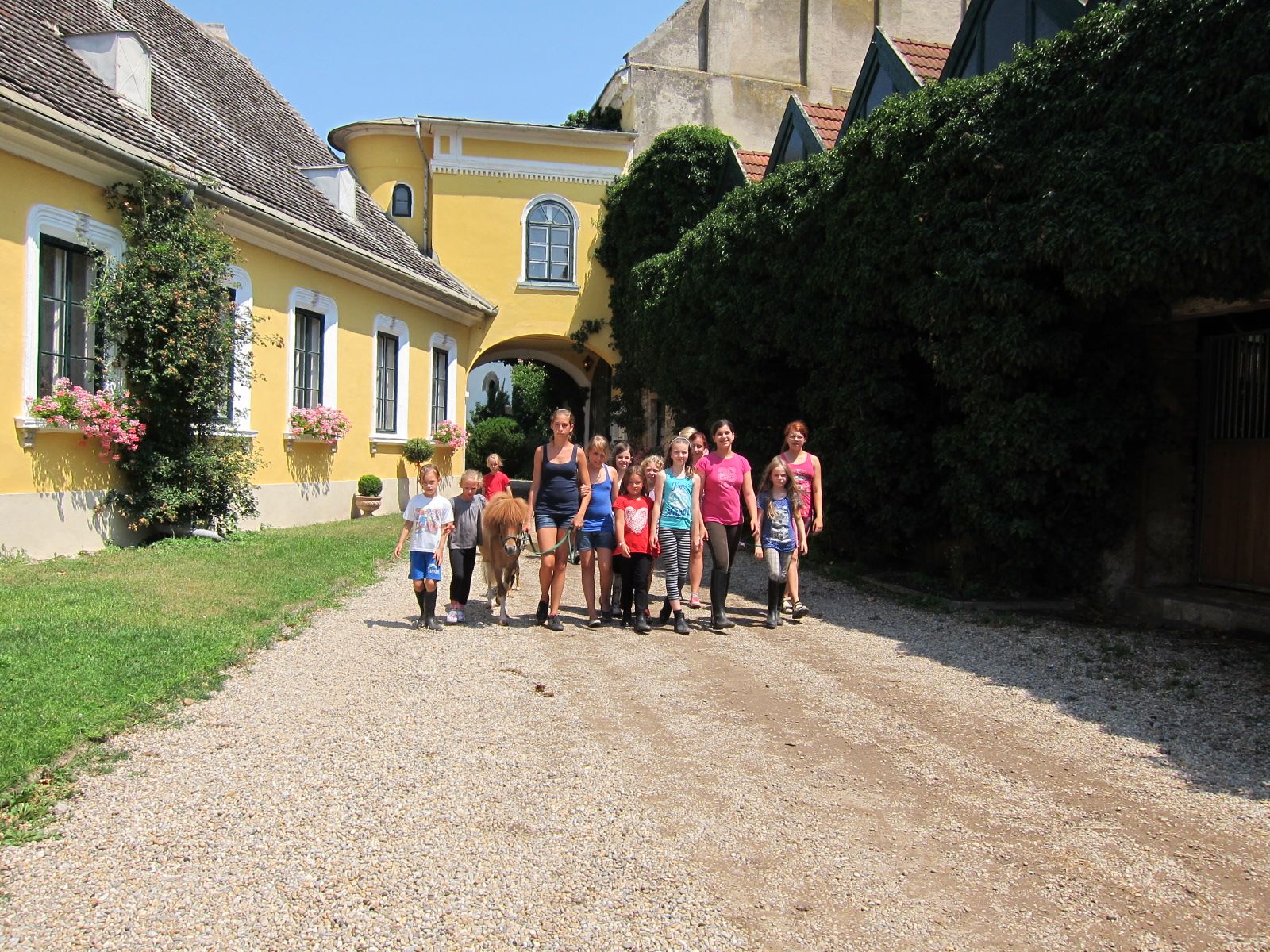 Group of children and adults with pony in front of yellow building.