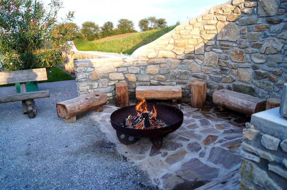 Barbecue area with fireplace and wooden benches in front of a stone wall.