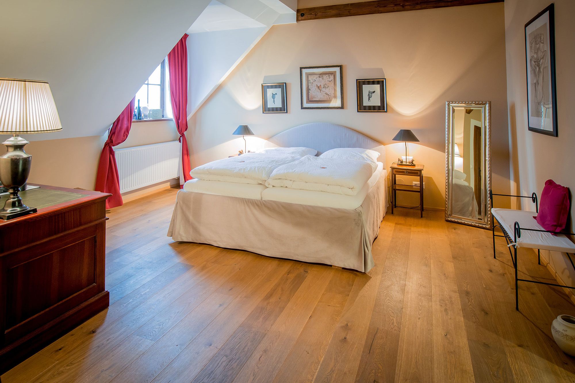 A cozy double room with wooden floor, a large bed, red curtains and stylish decorations.