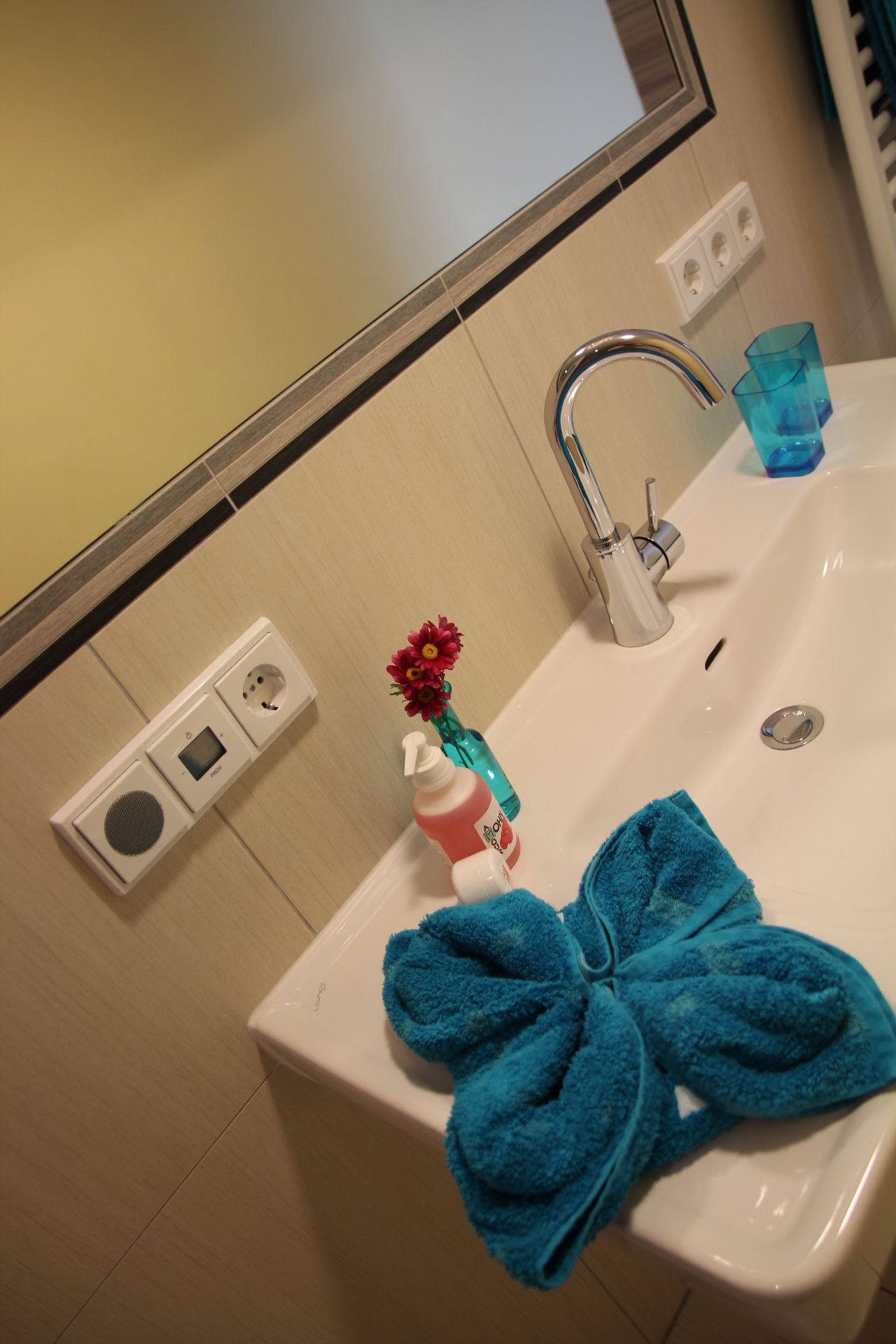 Washbasin with blue towel, soap dispenser and vase with flowers.