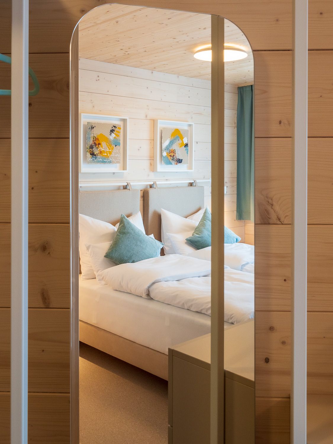 A cozy double room with wood paneling, two beds, blue pillows and modern art on the wall.