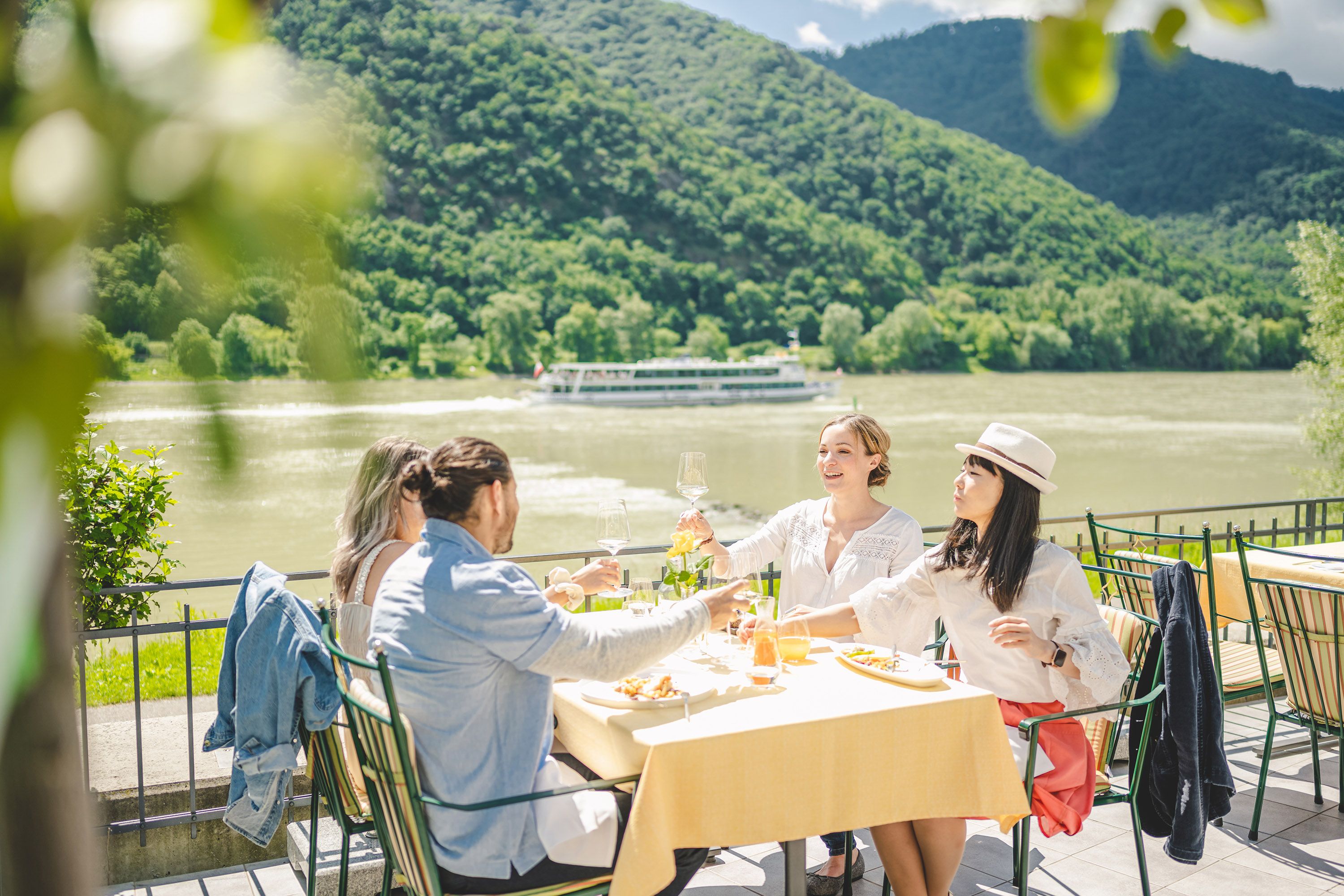 Four people sitting at a beautifully laid table on a terrace with the Danube and a ship in the background