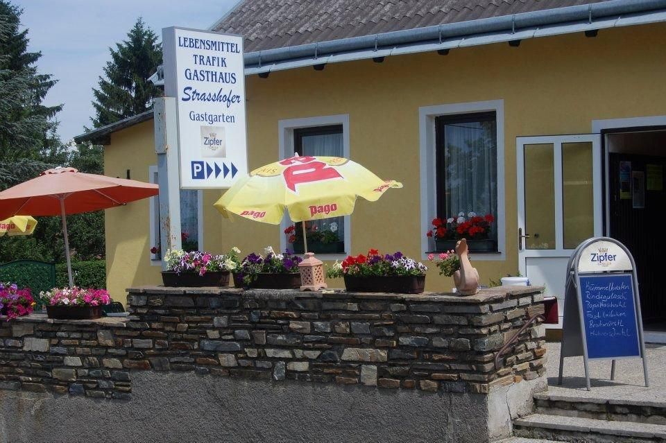 Exterior view of a yellow building with signs for food, tobacconist and inn. There are parasols and flowers in front of the house.