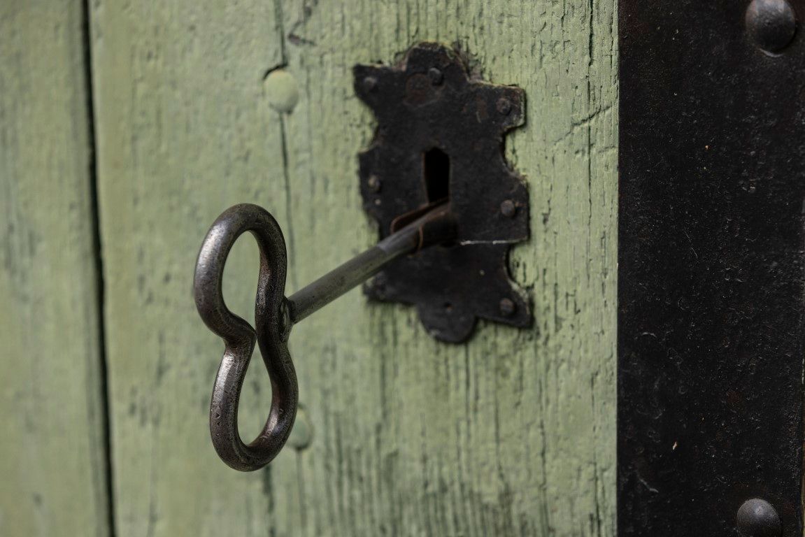 Close-up of an old key in a green wooden door lock.