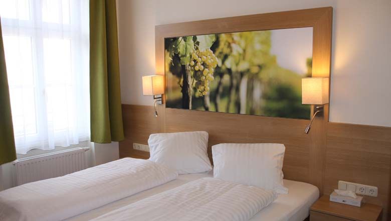 A cozy guest room with two single beds, a large picture of grapes above the bed and two wall lamps.