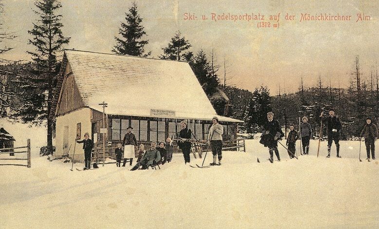 Historical postcard of a ski resort with people on skis in front of a hut in the snow.