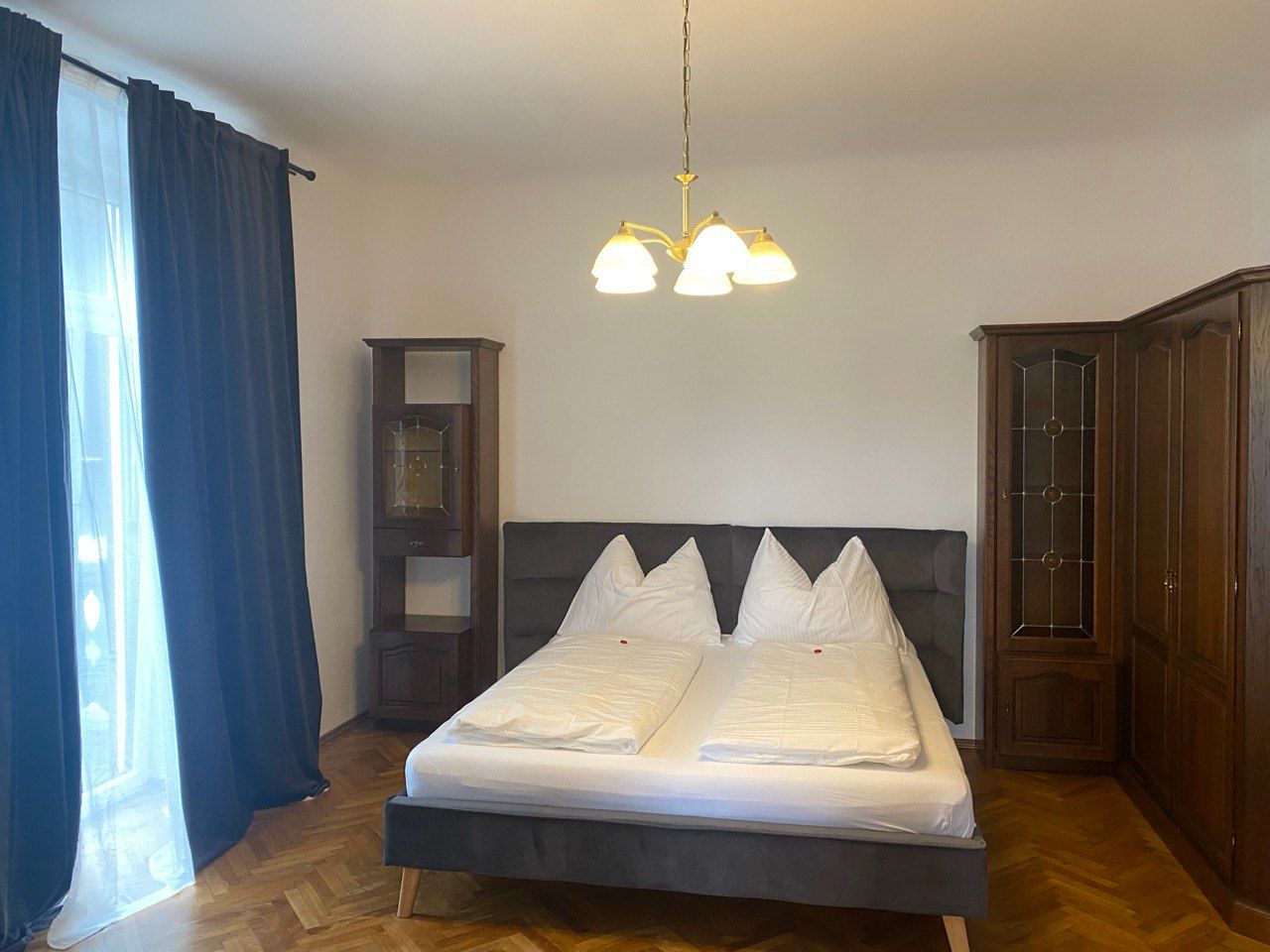 Bedroom with double bed, dark curtains and wooden wardrobes.