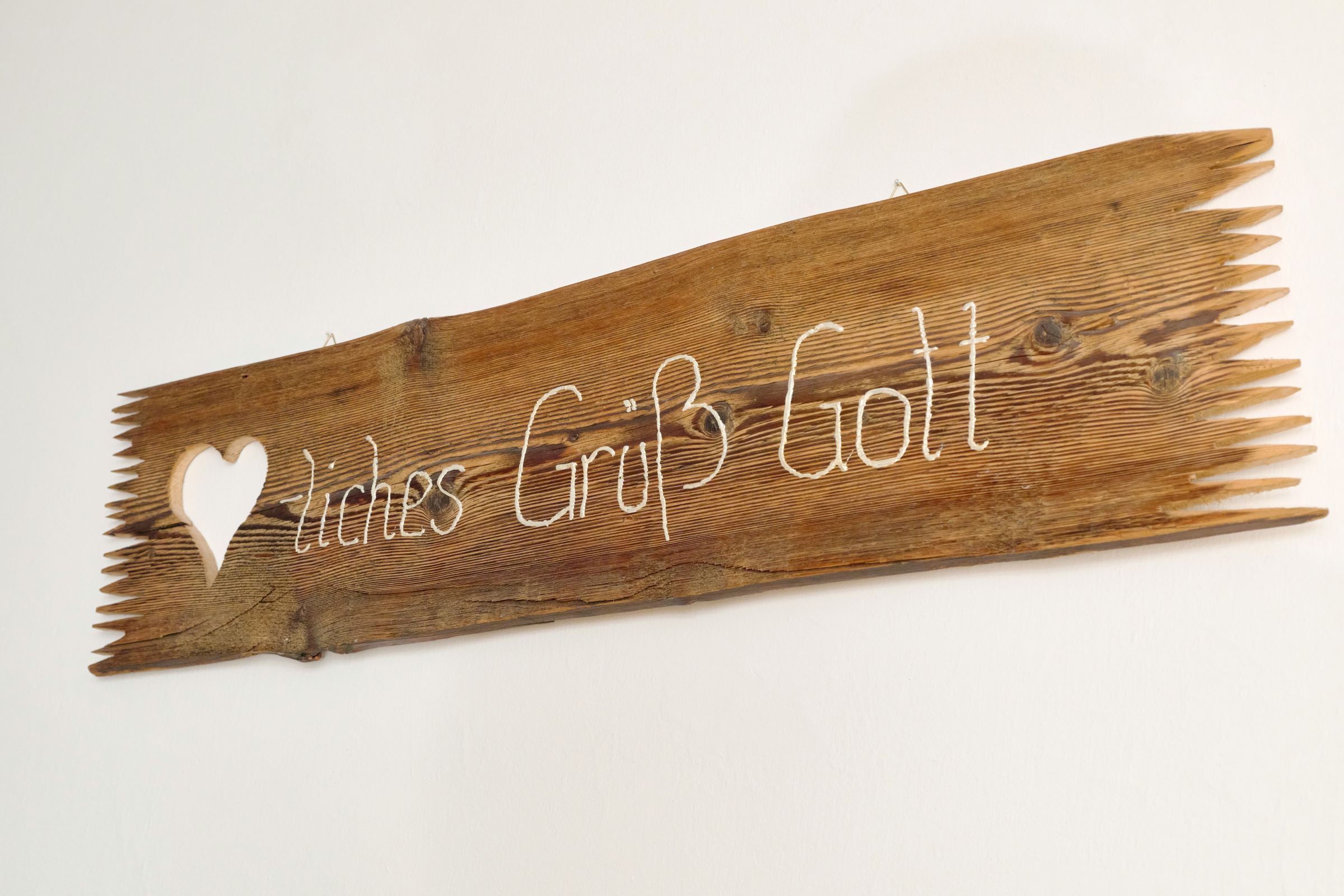 Wooden sign with the inscription 'Herzliches Grüß Gott' and a heart symbol.
