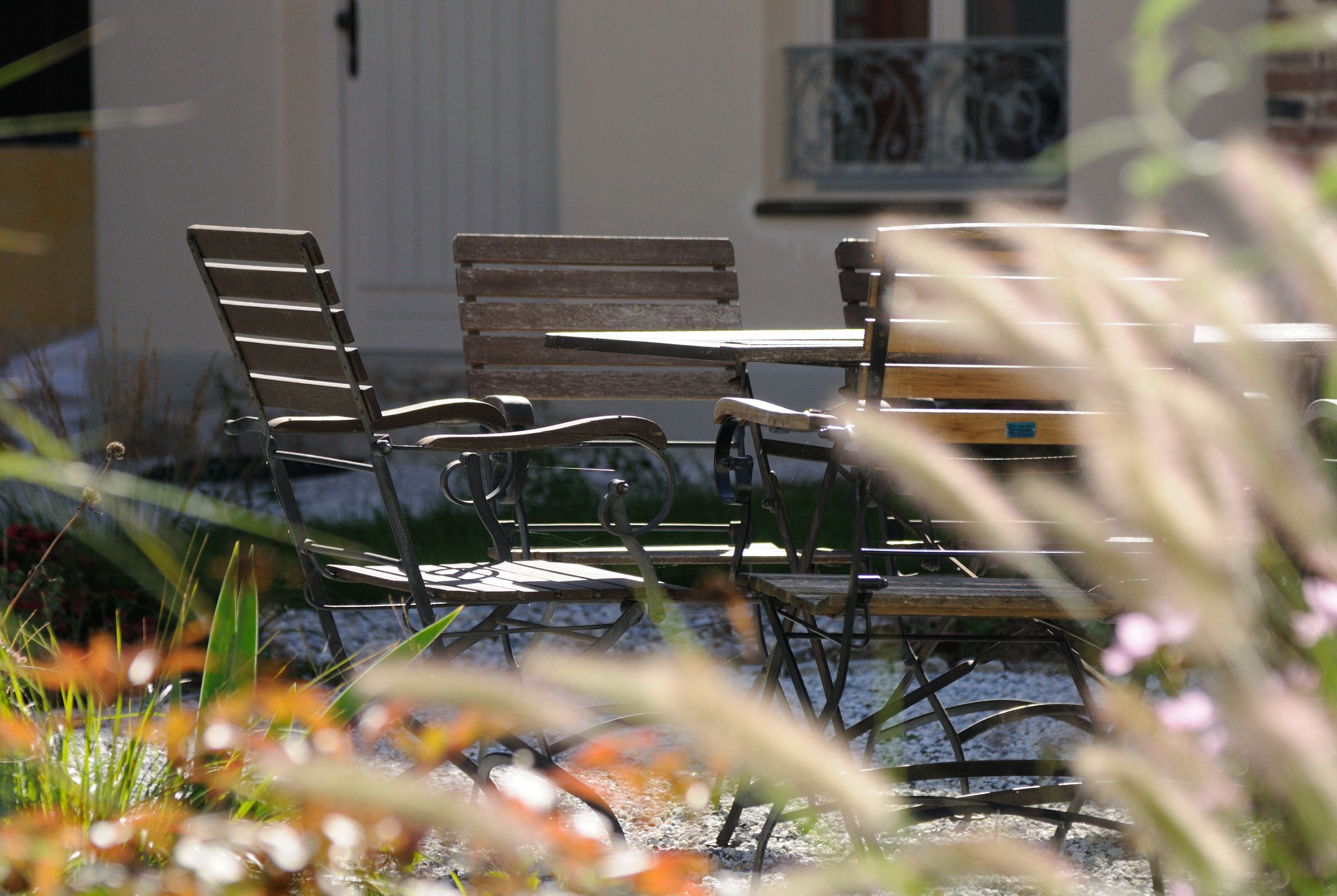 An inner courtyard with a table and chairs made of wood and metal, surrounded by plants and a building in the background.