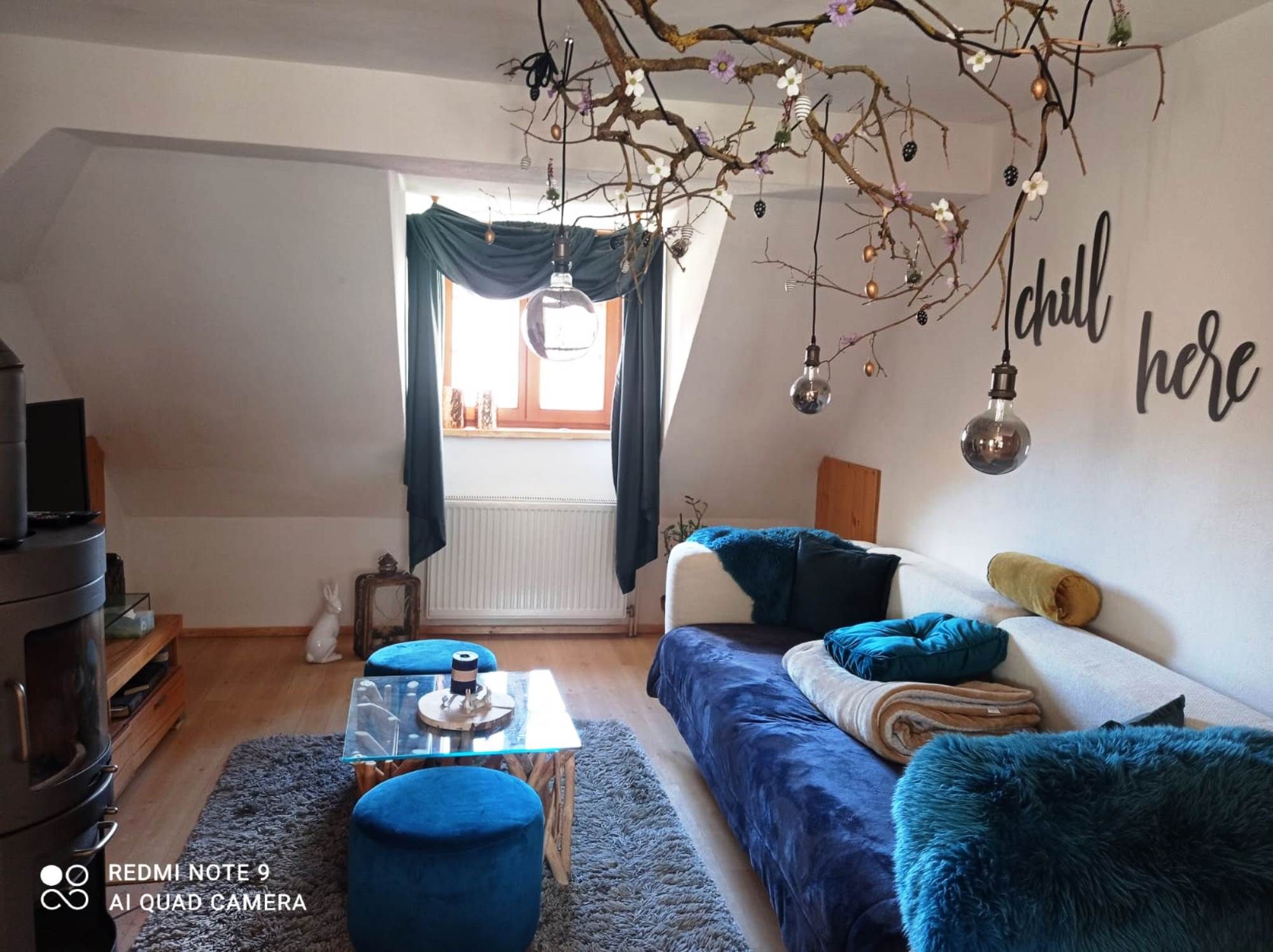 Cozy living room with sofa, blue carpet, decorative branches and 'chill here' lettering.