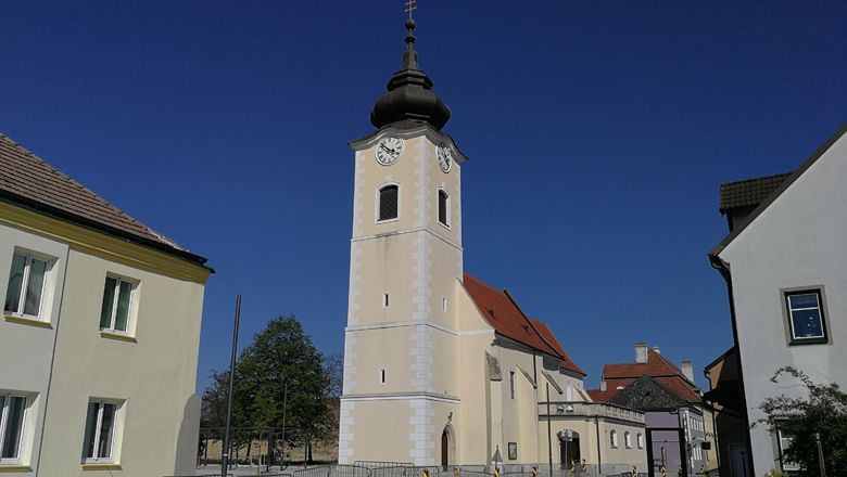 Church with tower and clock in Rohrendorf against a blue sky.