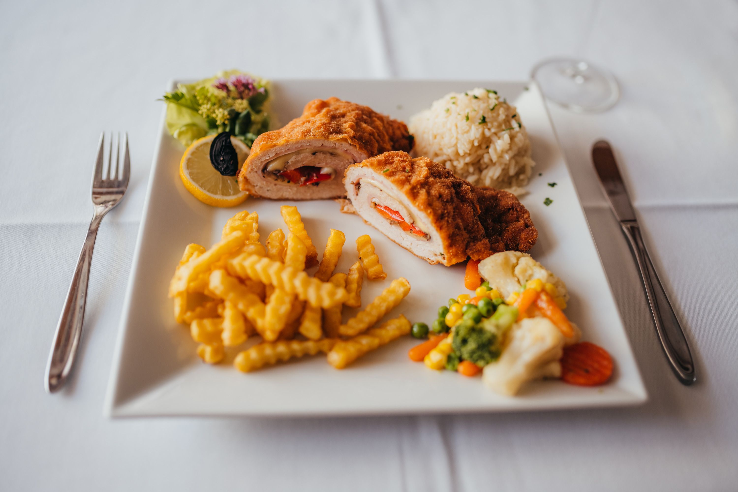 Baked chicken with fries, rice and vegetables on a white plate.