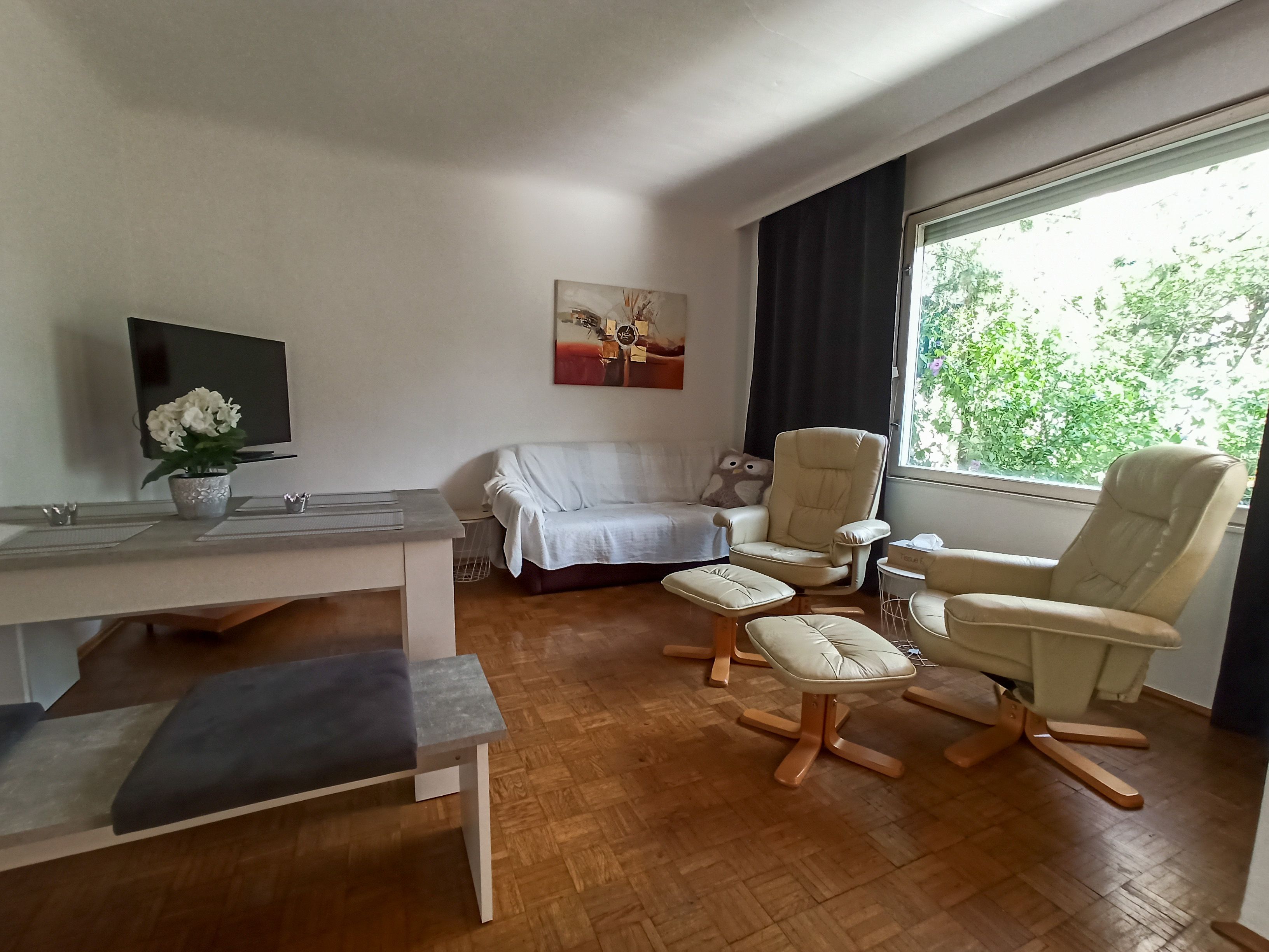 Living room with sofa, two armchairs, table and large window.